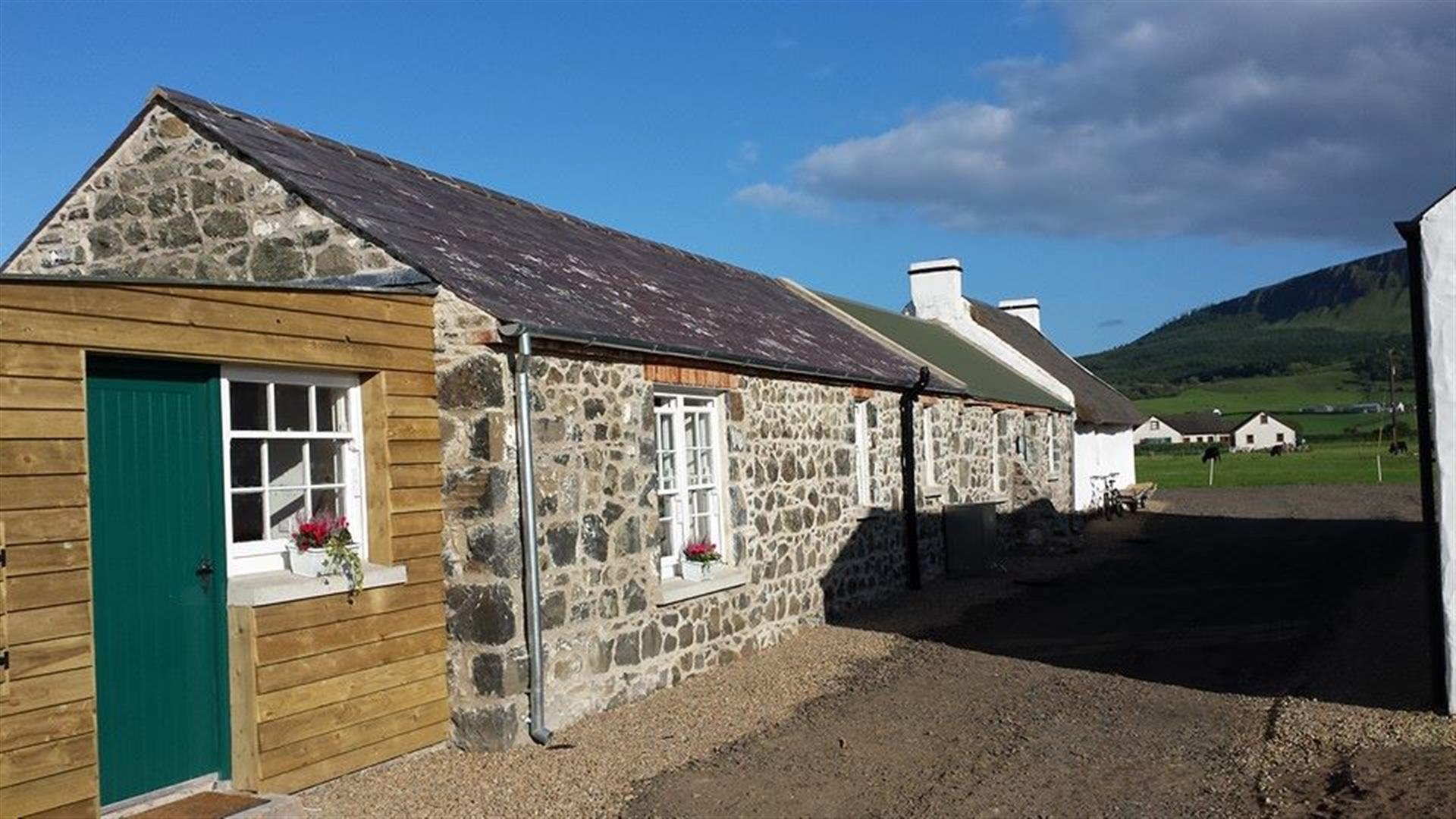 Front exterior view of a stone and wooden cottage connected to other cottages.