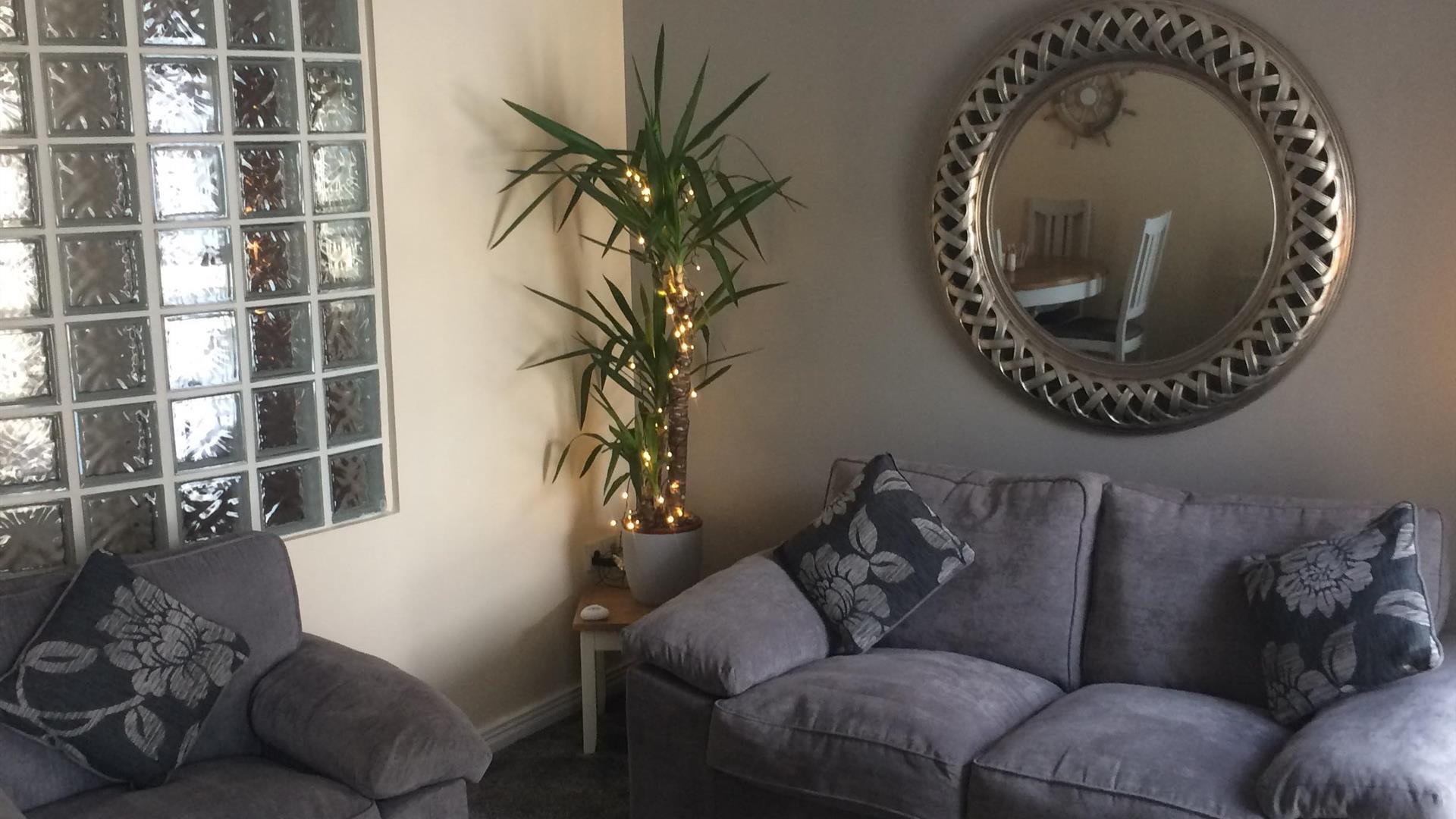 a photo showing a living room with sofas, a mirror, a plant and a window