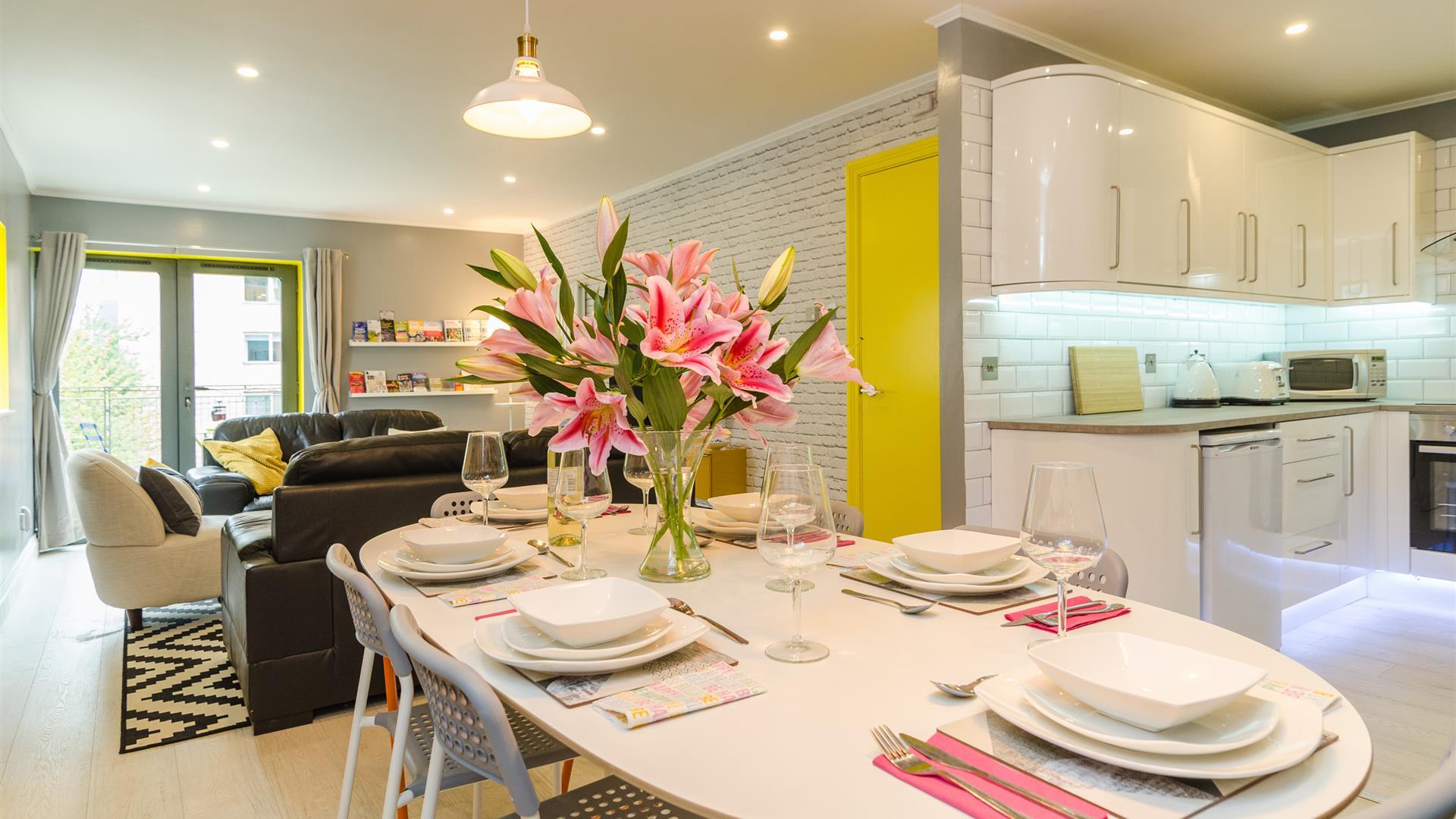 An open plan living space with a sitting room, kitchen and a dining room with a table with flowers.