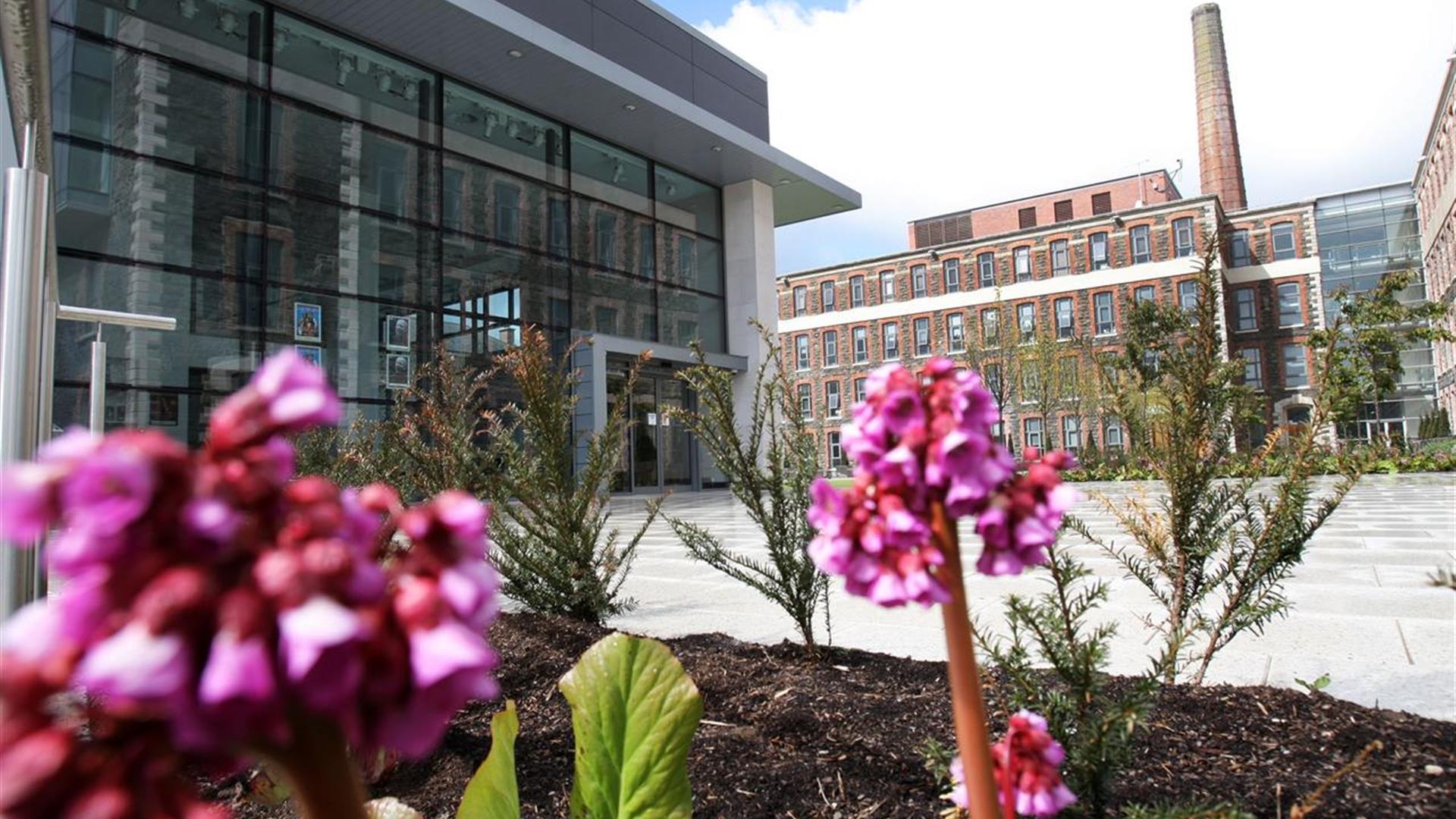 Exterior of the Theatre At The Mill with a flowerbed and pink flowers.