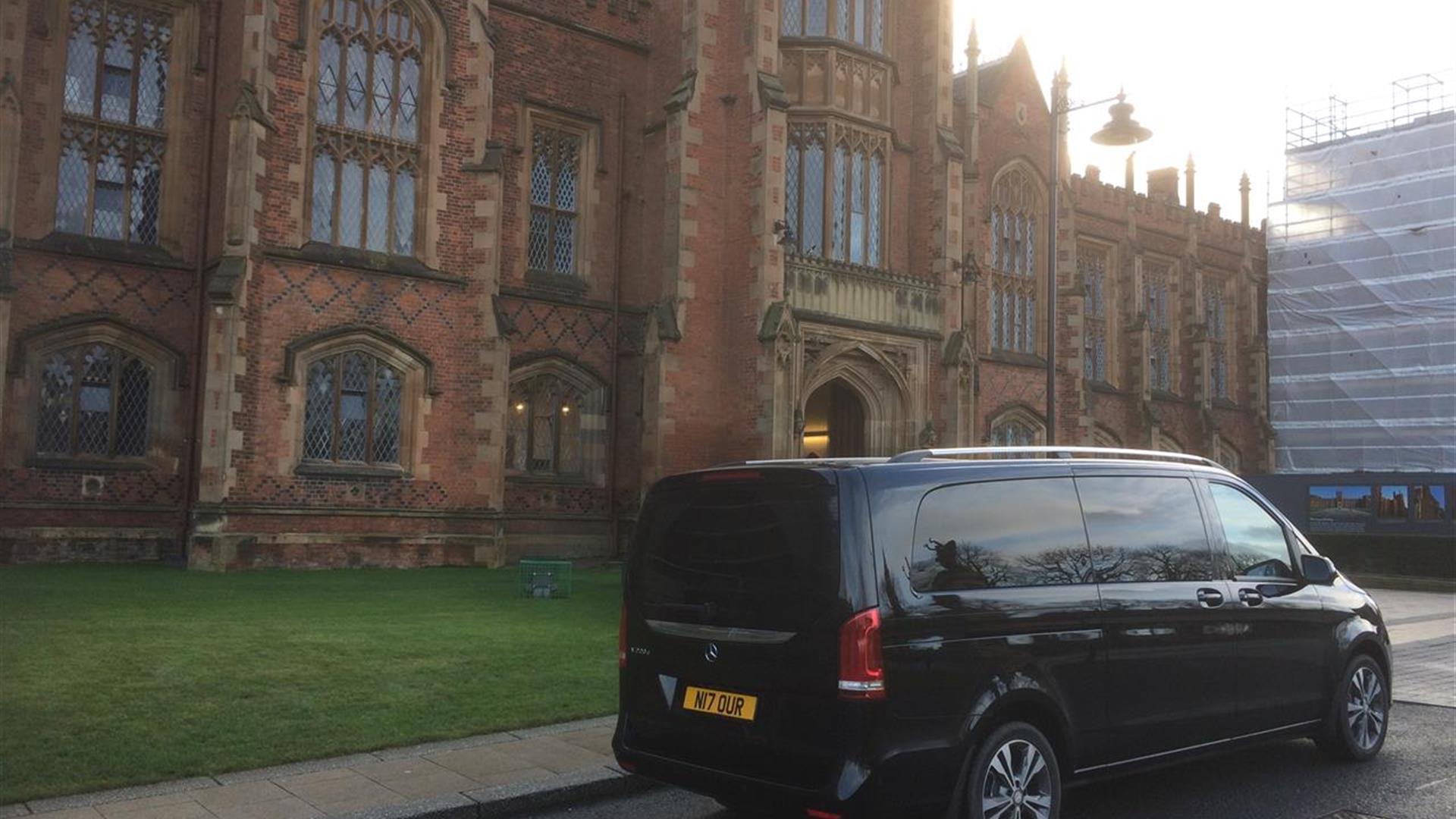 A black tour van parked outside Queens University's Lanyon building.