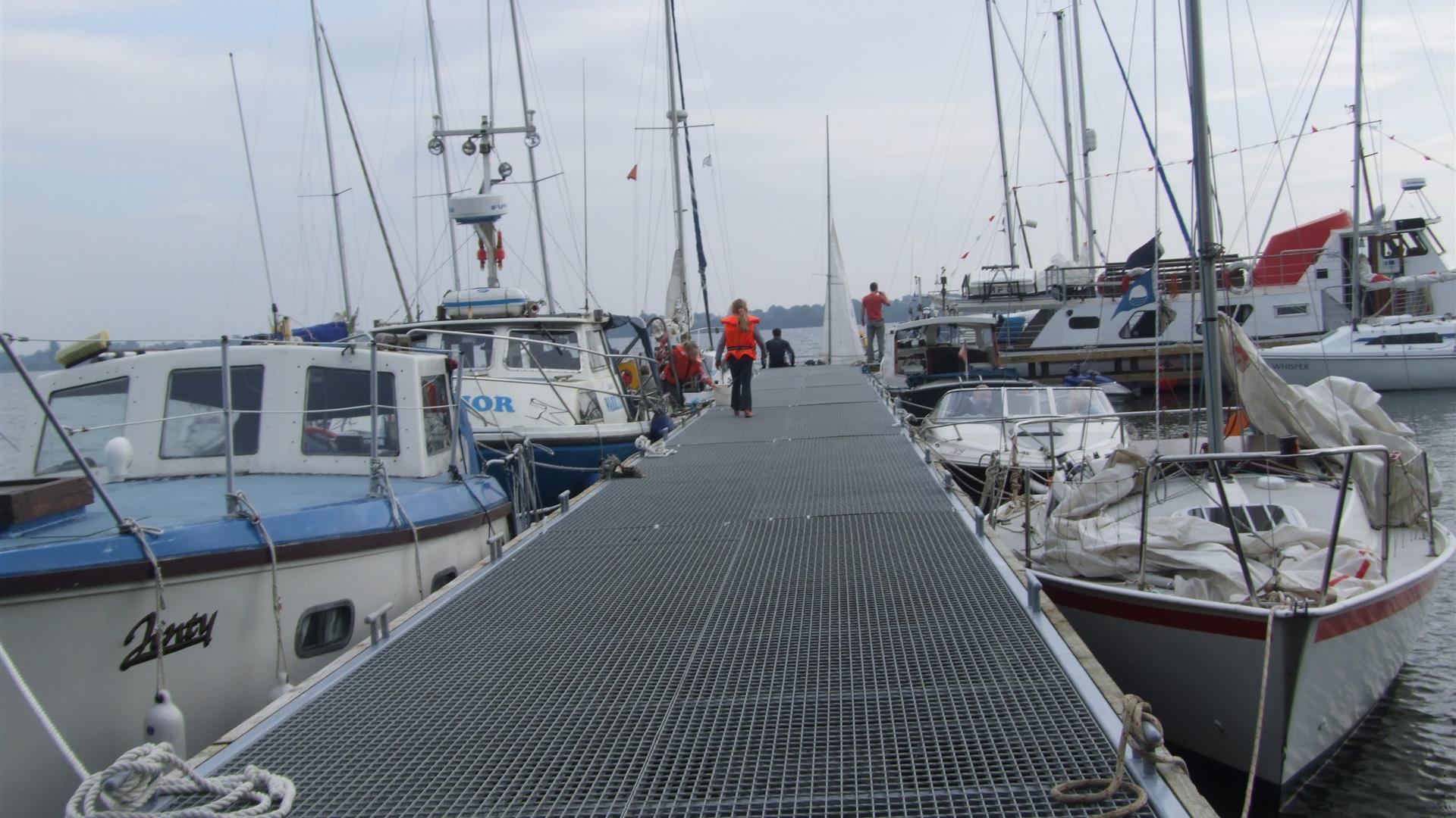 Image shows a walkway and various types of boats in a marina