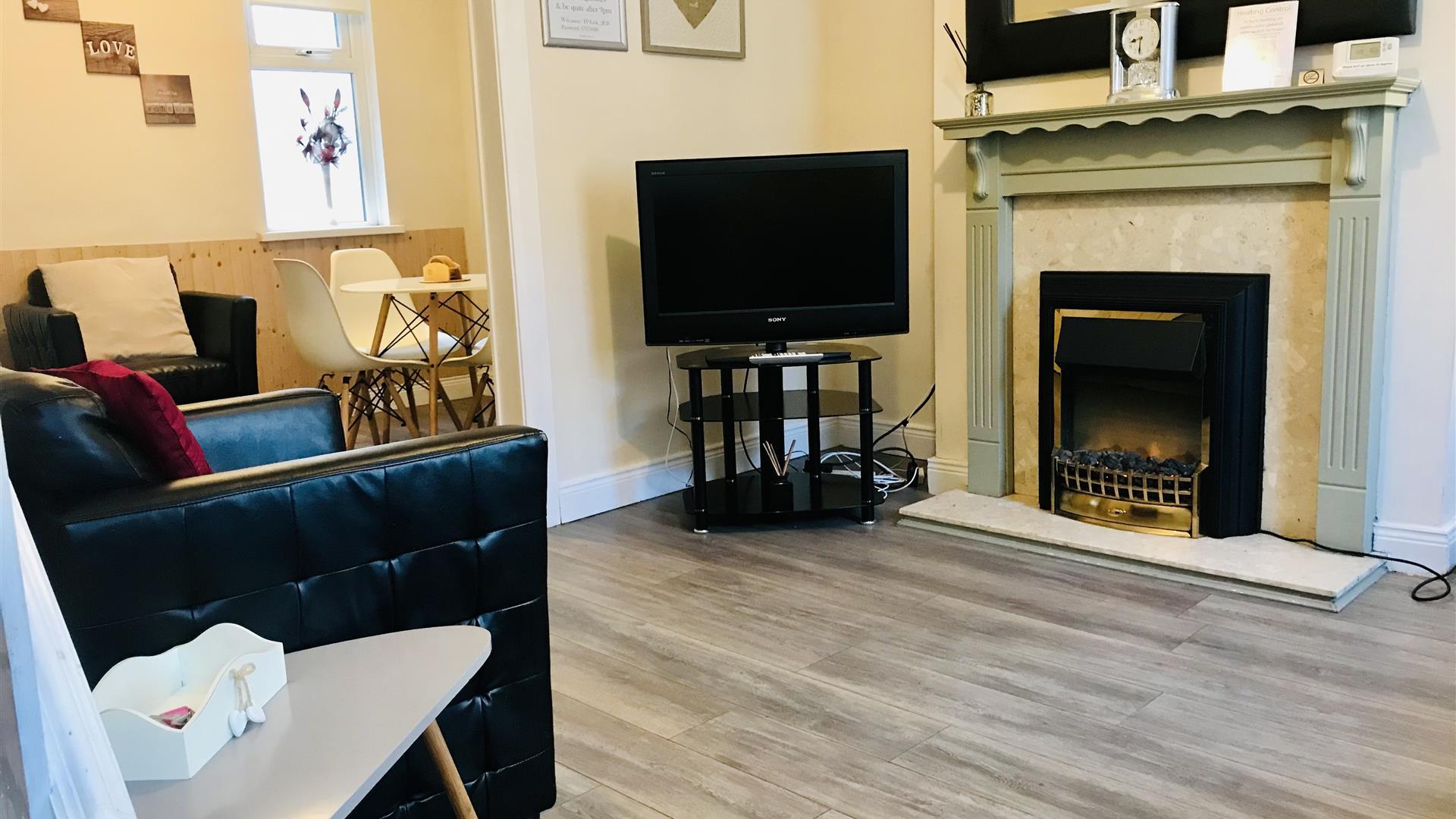 A living room with a fireplace, chair and TV leading to a dining area.