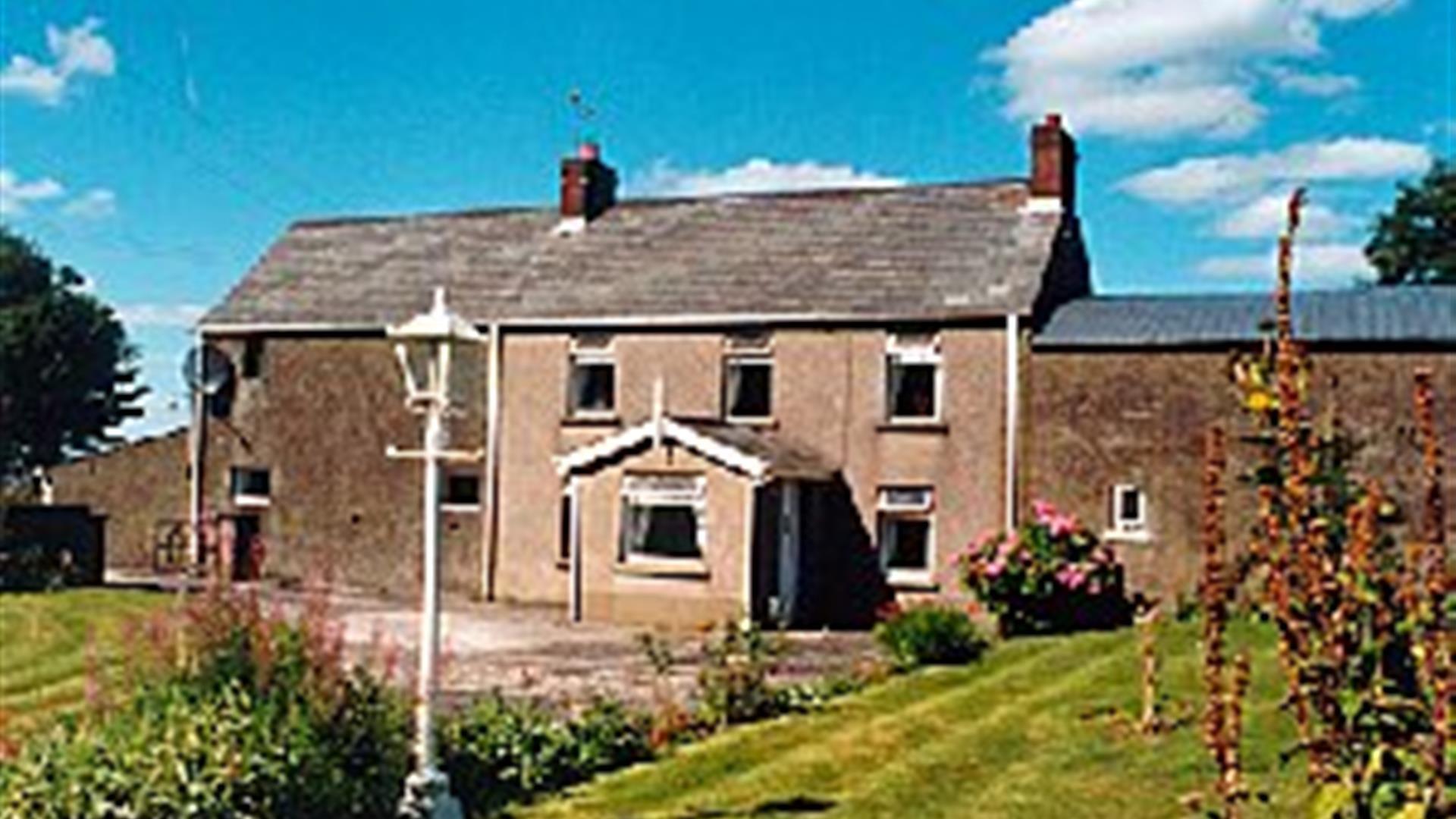 A large farmhouse with a front garden filled with flowers and a lamp.