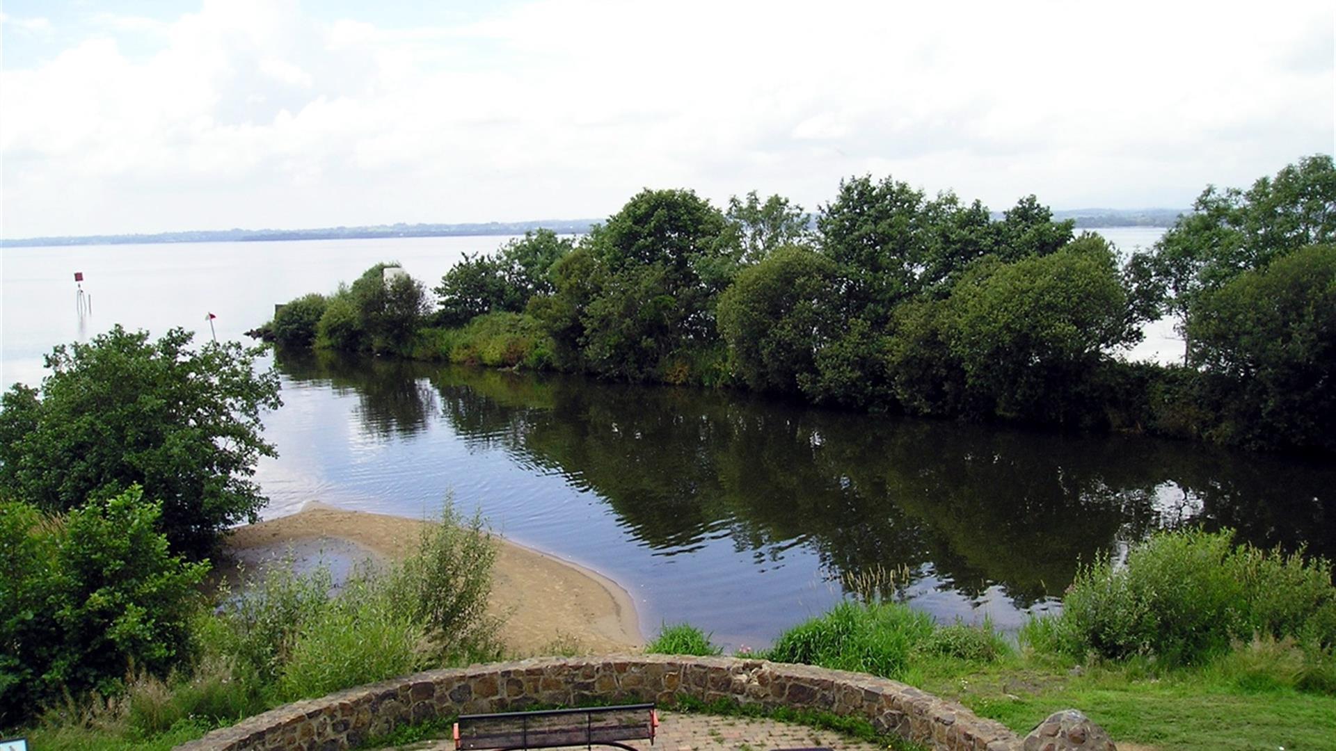 A stone area with a bench with a view at the end of the canal reaching the lough.