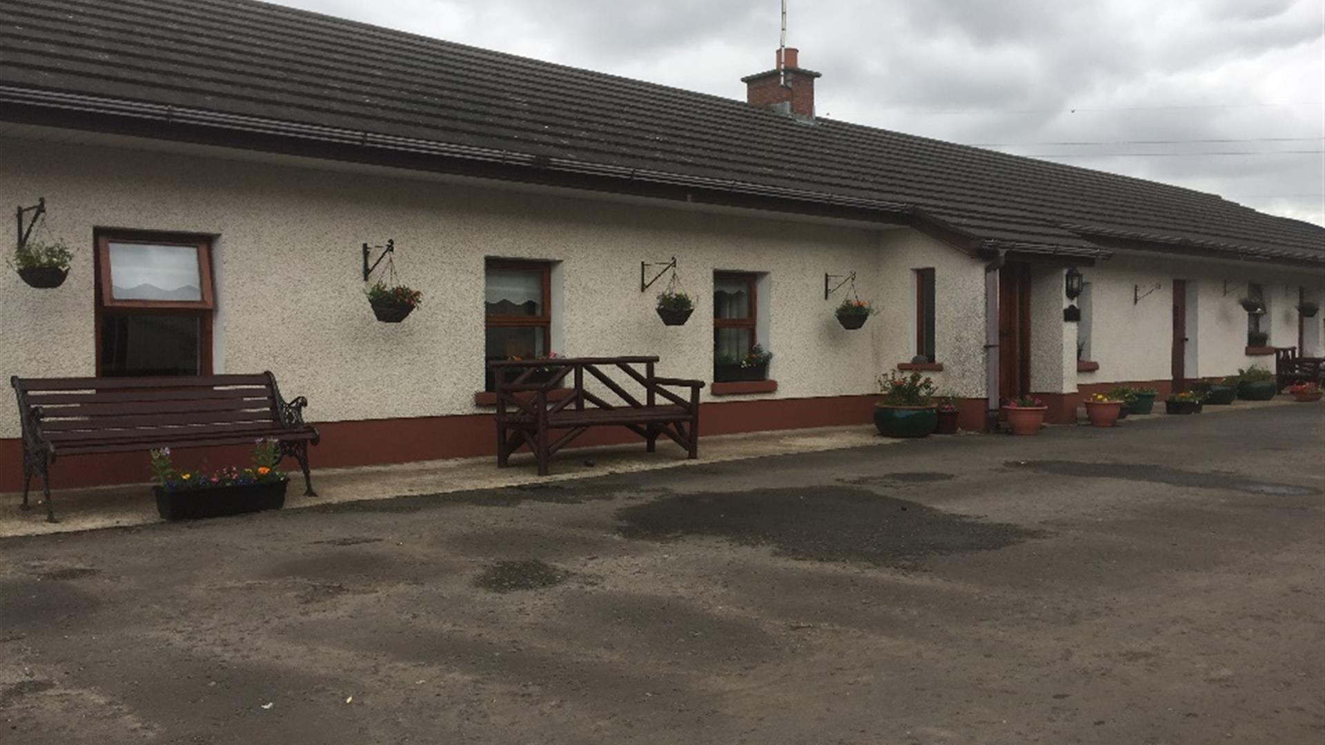 Image shows outside of cottage. Wooden benches outside. Gravel driveway.