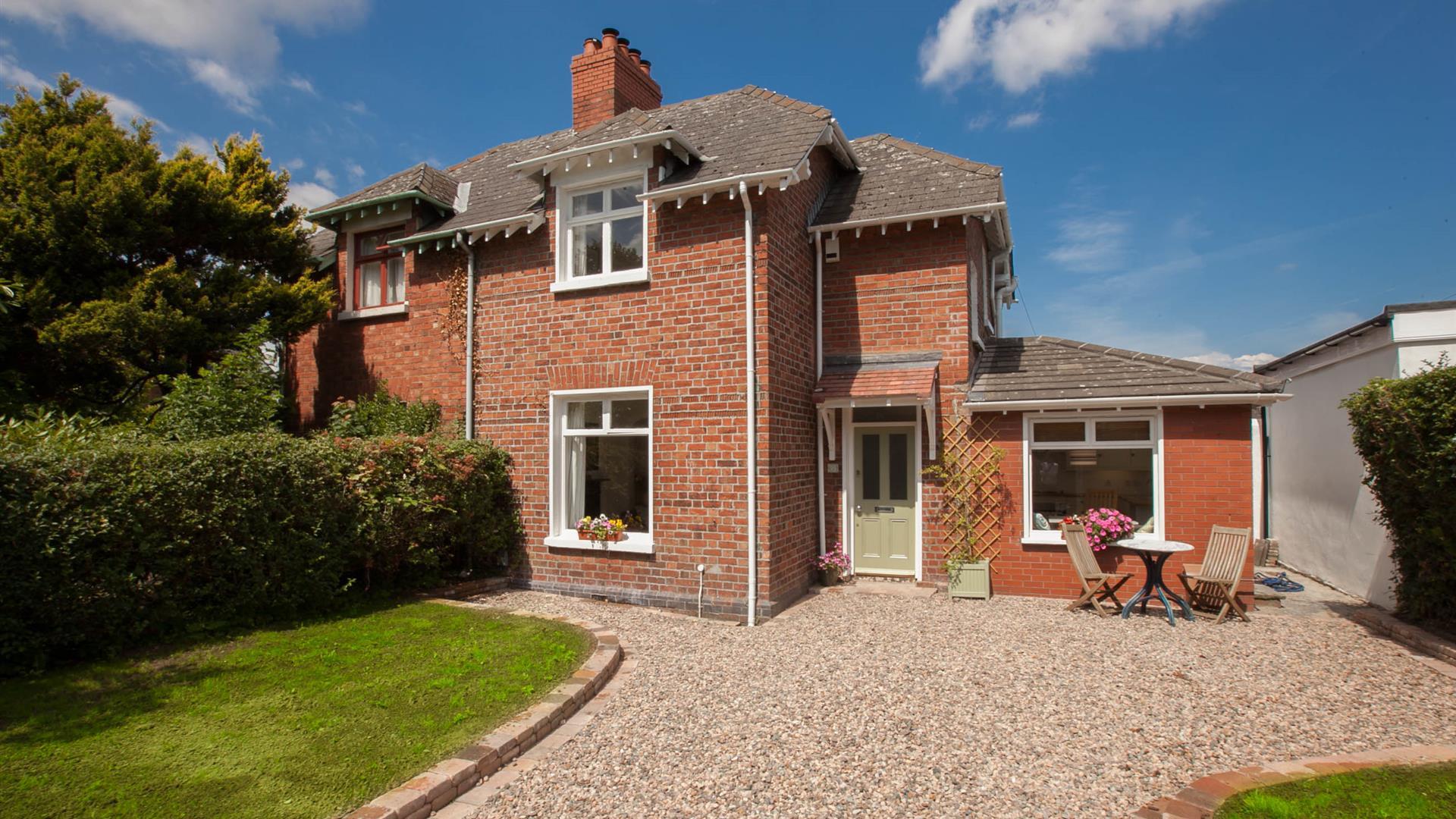 exterior of a semidetached cottage with a stone driveway, a lawn and some garden furniture.