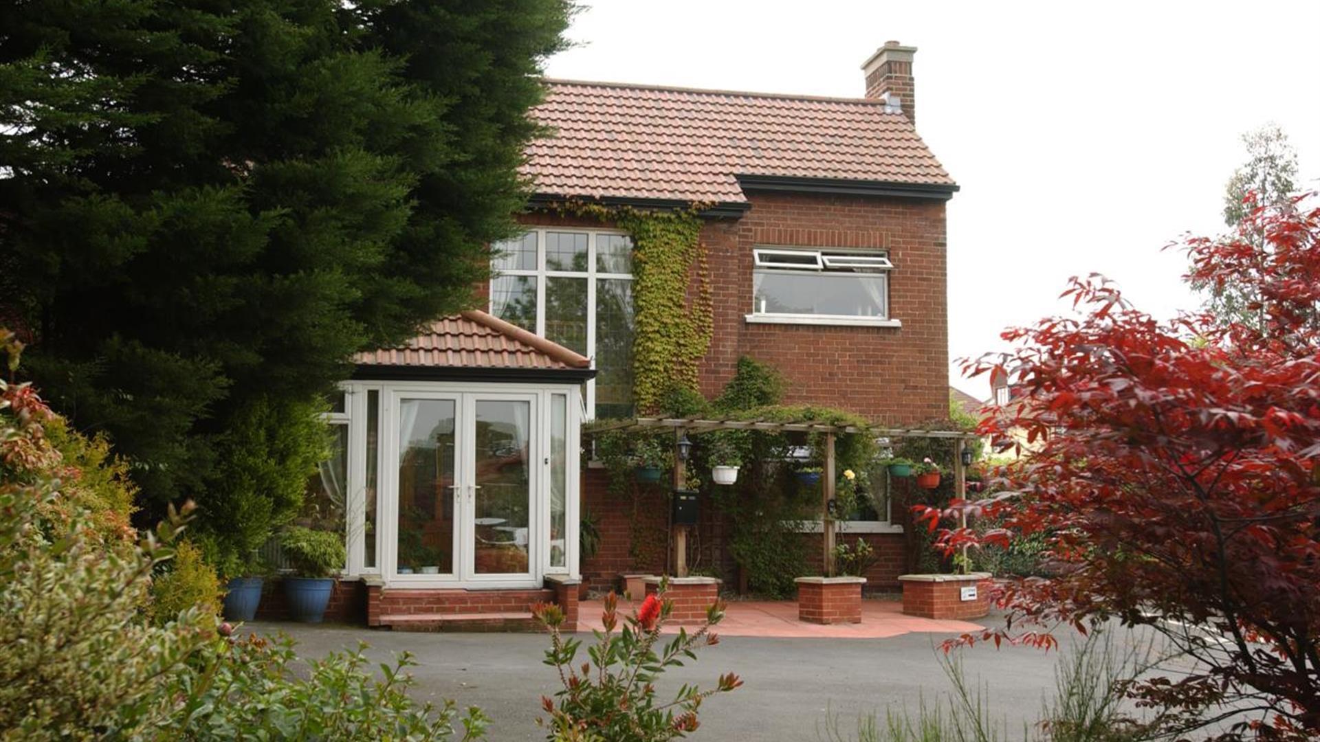 A B&B seen through a colourful garden of trees, bushes and flowers.