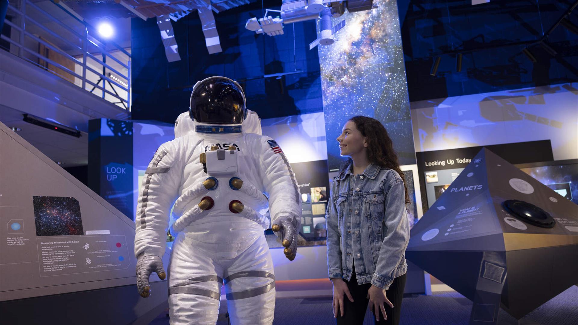 Girl smiles at life size model of astronaut suit