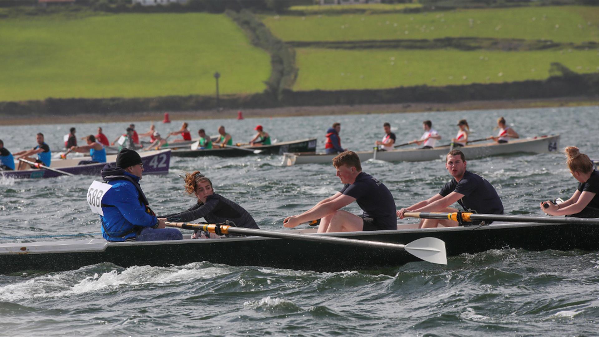 Number of rowers in rowing boats in the sea competing in a race, with shore in background