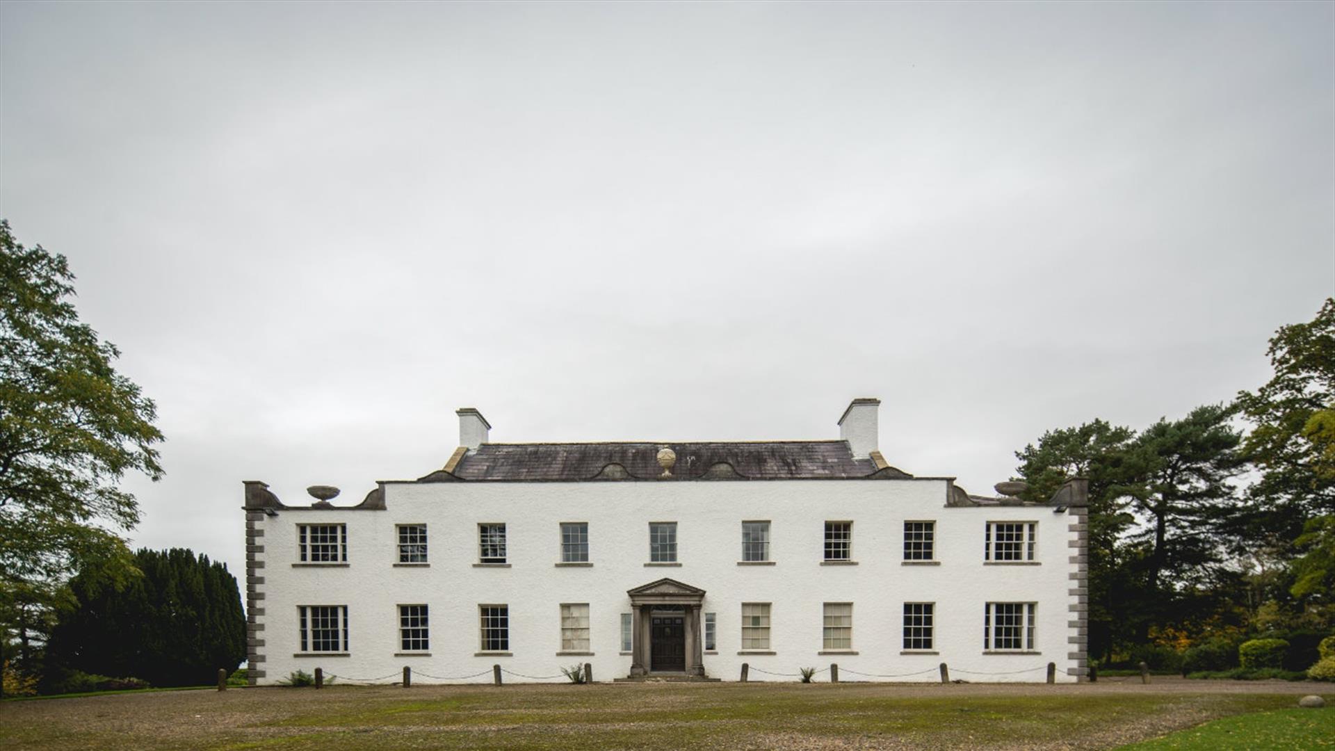 Elegant 17th-century National Trust property, Ardress House, with its distinctive Georgian facade and well-manicured lawns and trees, located near Craigavon, Northern Ireland.