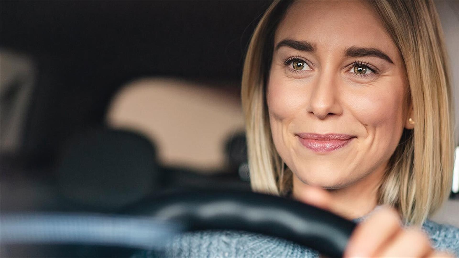 A smiling woman with her hands on the steering wheel of a car.