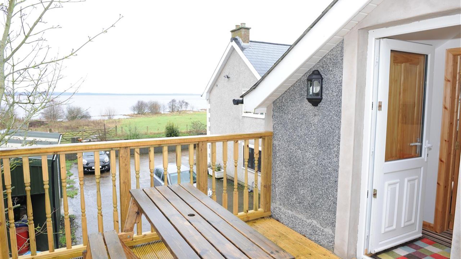 A decked entrance to a second story loft cottage with a picnic table and a view of a lake.