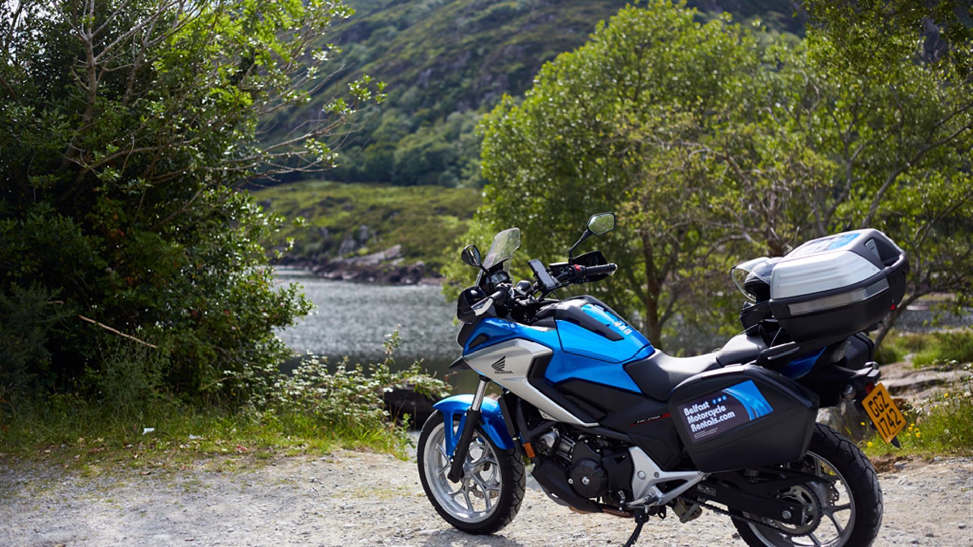 Image shows motorcycle parked at scenic area with view of river between trees