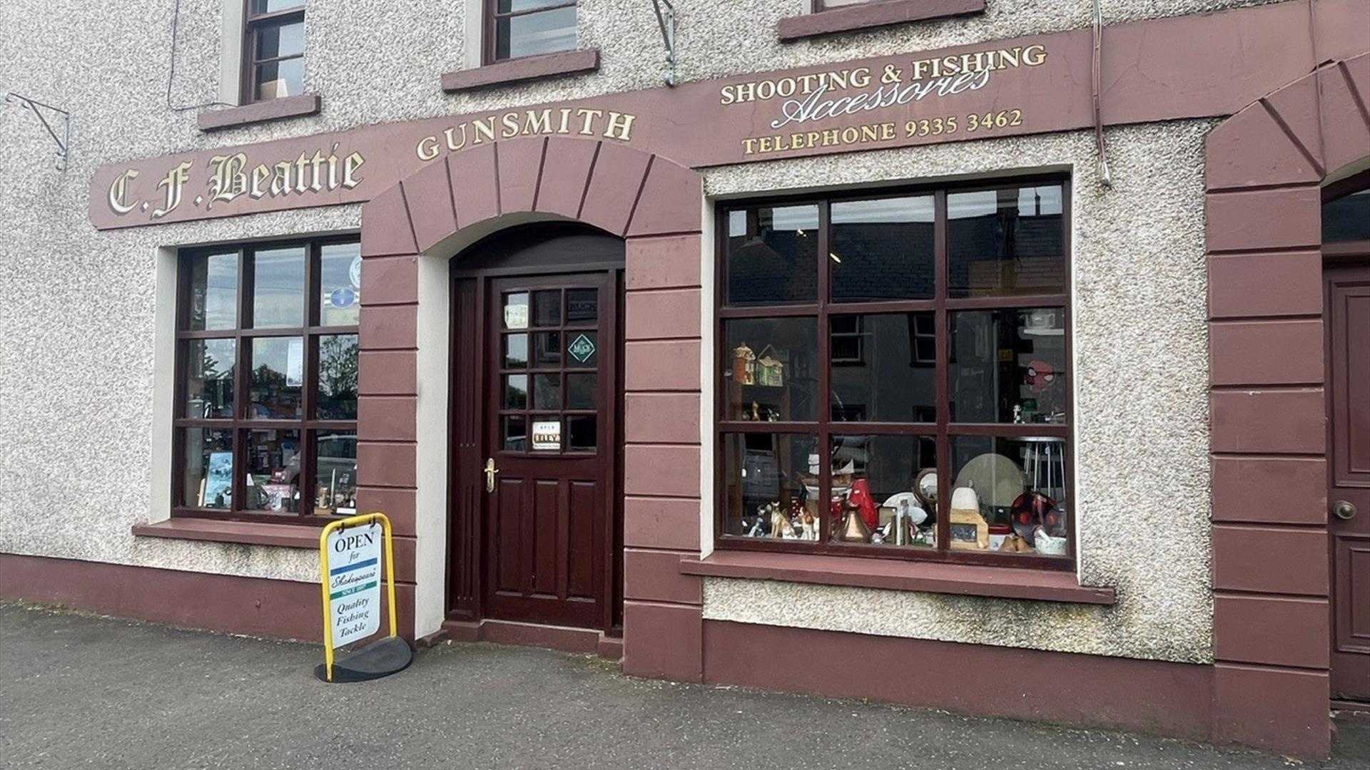 Brown and cream exterior of CF Beattie with sign stating Shooting & Fishing Accessories / Gunsmith plus antique displays in windows