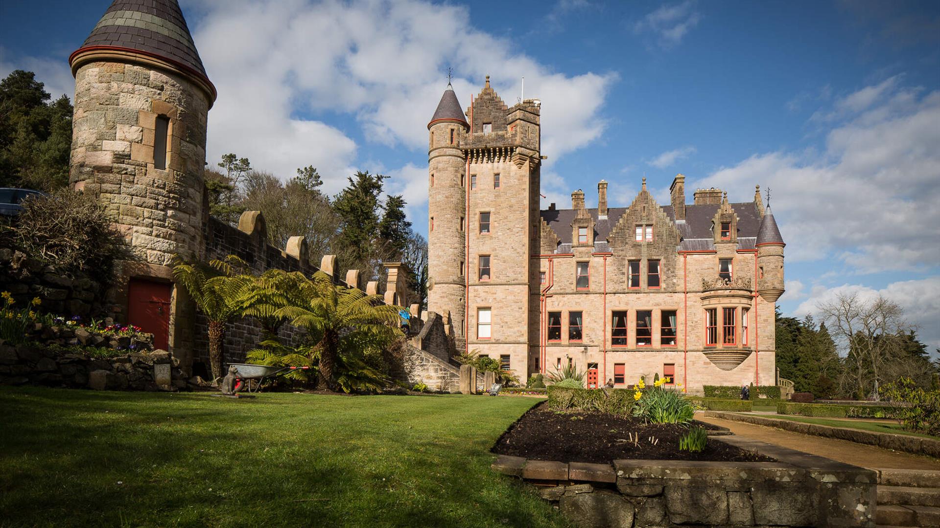 Belfast Castle, a grand sandstone estate, nestled on Cavehill overlooking the city of Belfast and Belfast Lough under a blue sky.