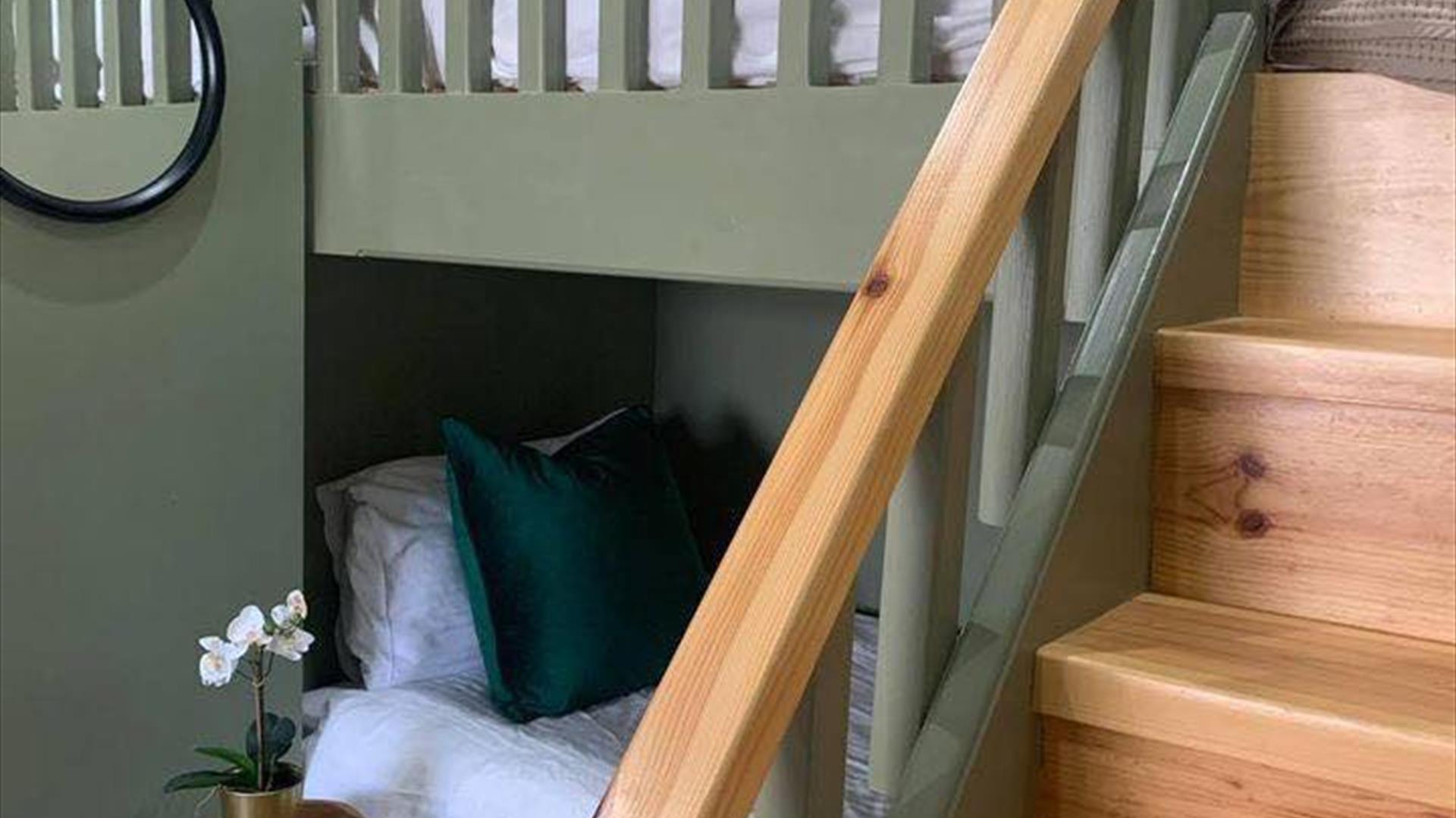 Image is of loft bedroom with bunk beds with wooden stairs up to top bunk