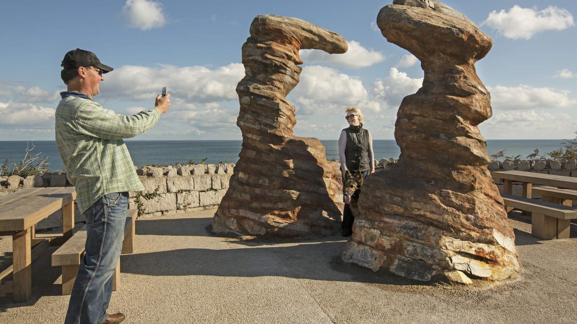 A man taking a photo of his wife who is standing besidee the 'Smugglers Head' Public Art at the Bloody Bridge in Newcastle.