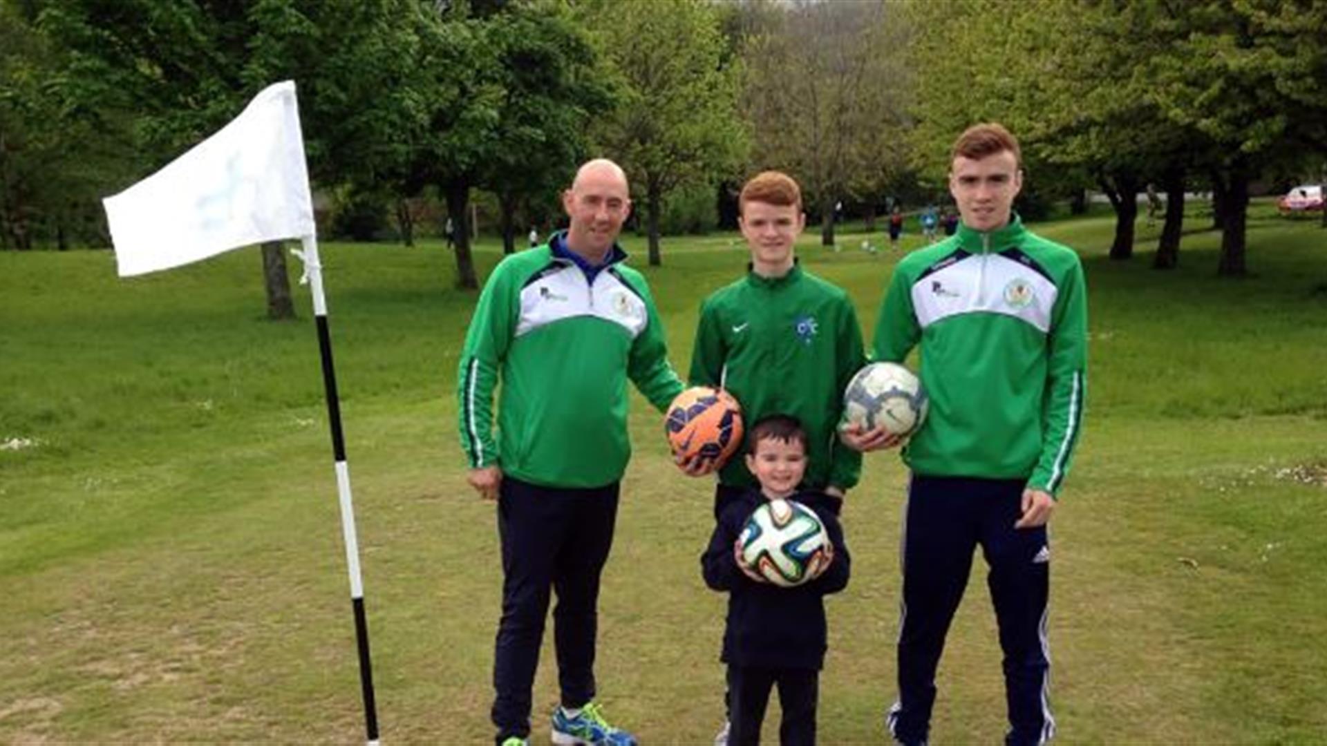 Image is adults and a child holding footballs on the golf course