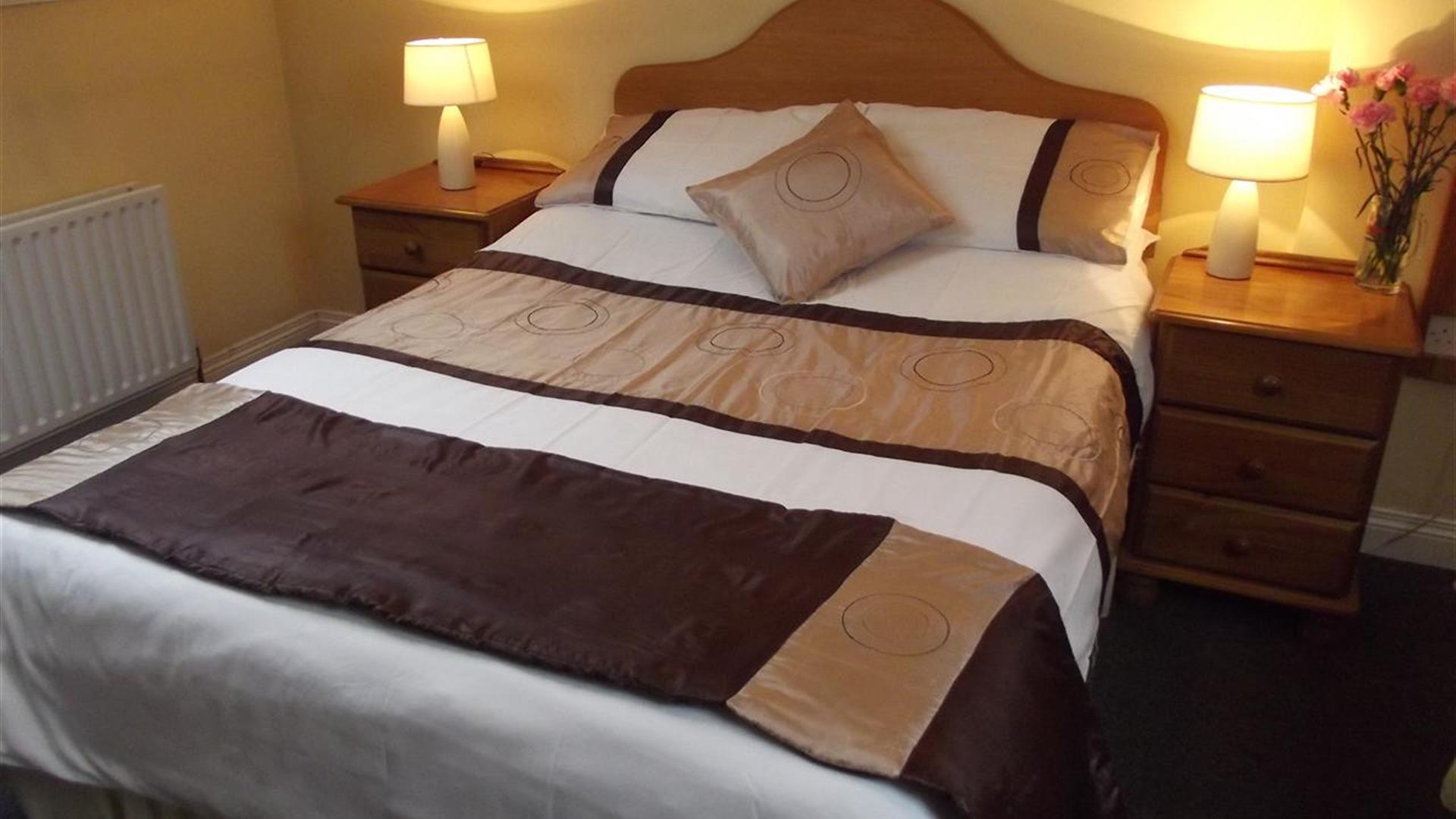 A double bedroom with a brown throw and pillows and nightstands with lamps and flowers.