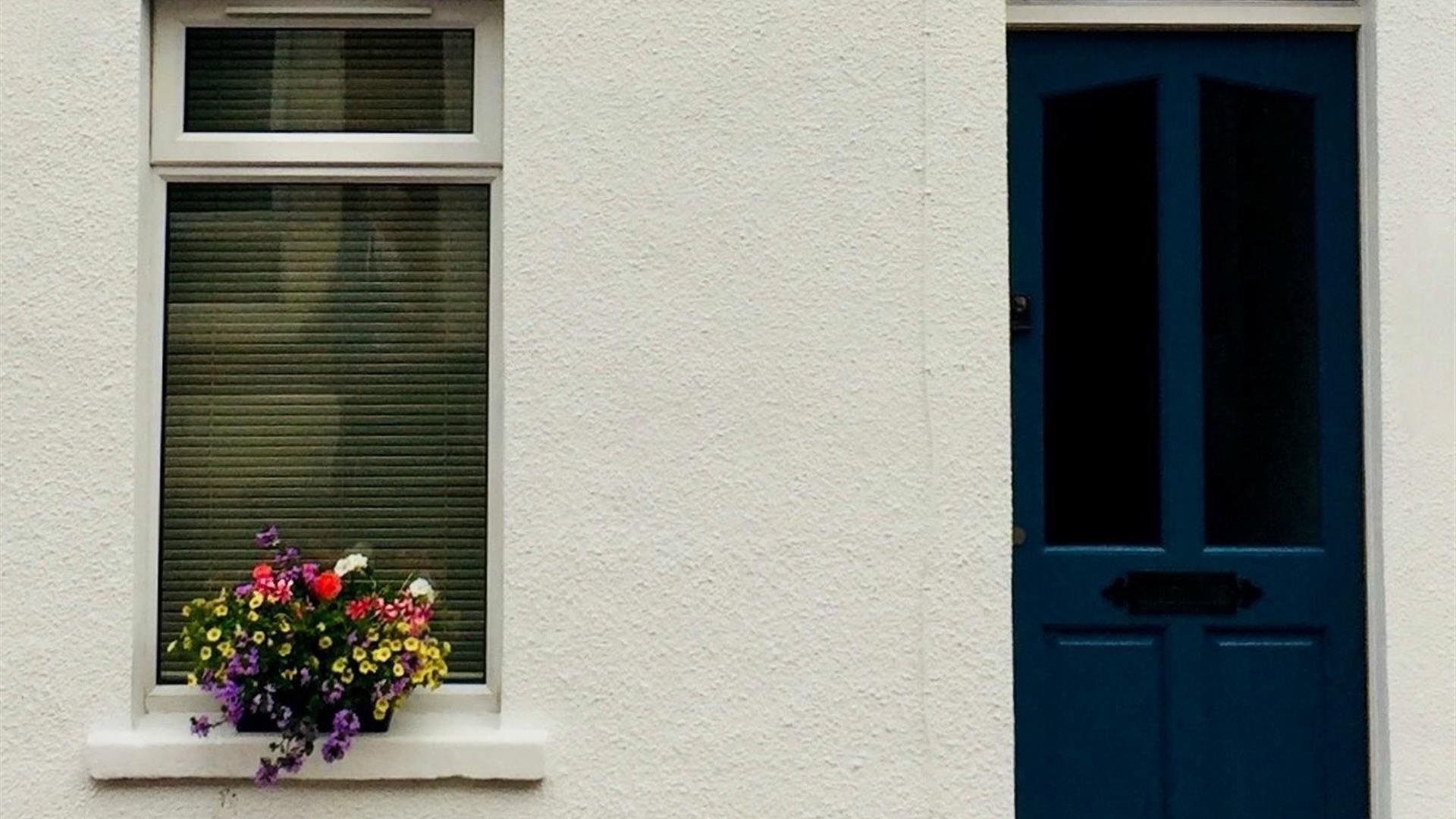 The front of a house with a dark blue door and a window decorated with flowers.