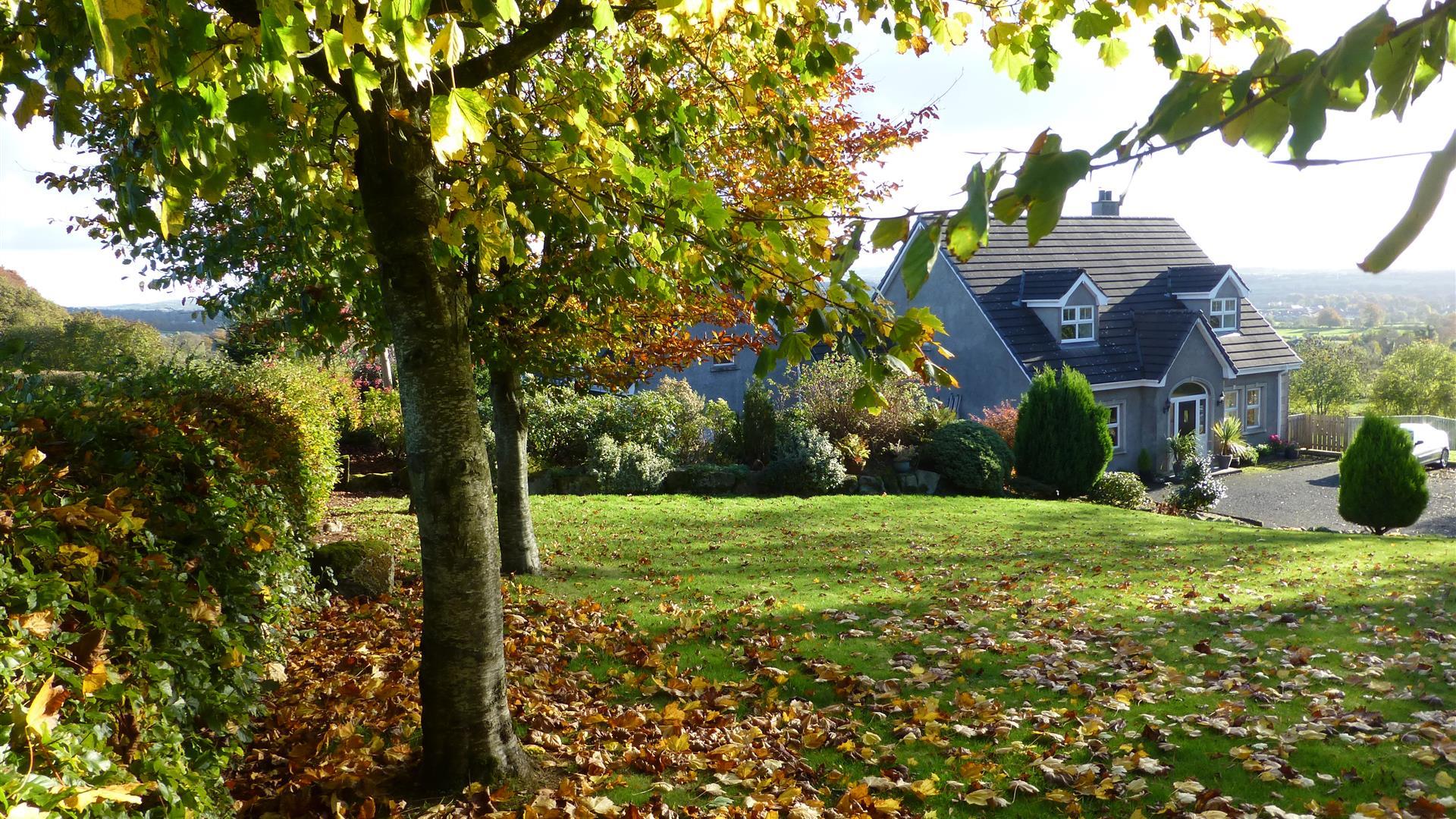 A lawn with falling leaves of a large grey house in the hills.