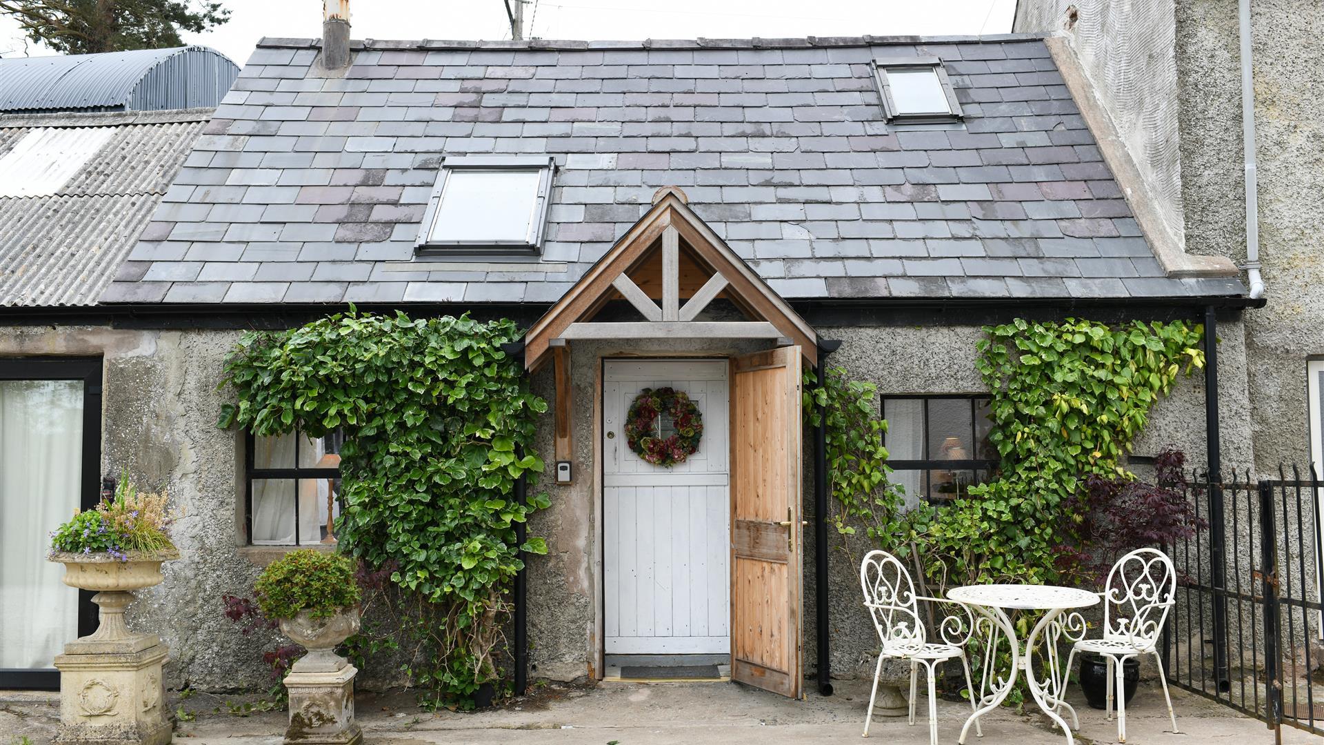 Outside view of Milk House with greenery on the walls and outside table and 2 chairs