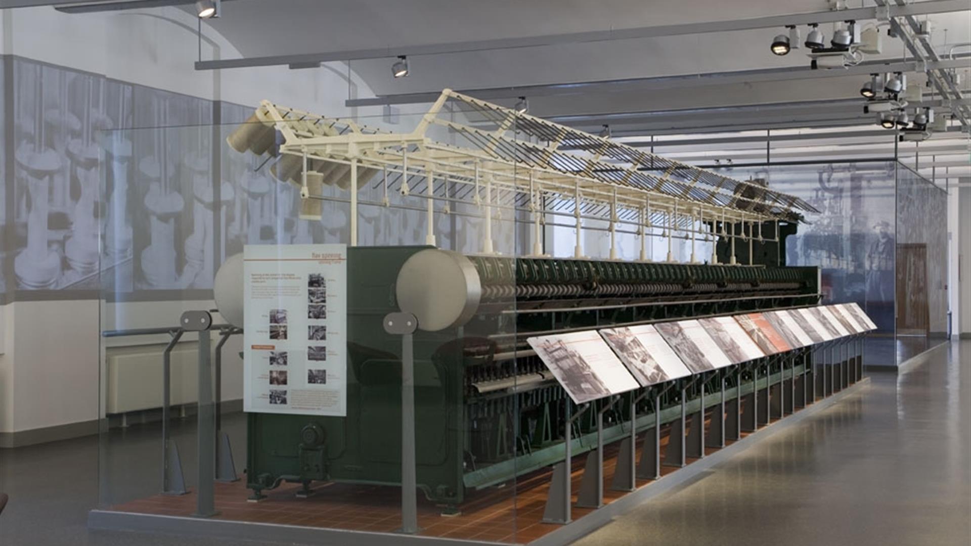 A large old spinning frame exhibit behind glass with information displays.