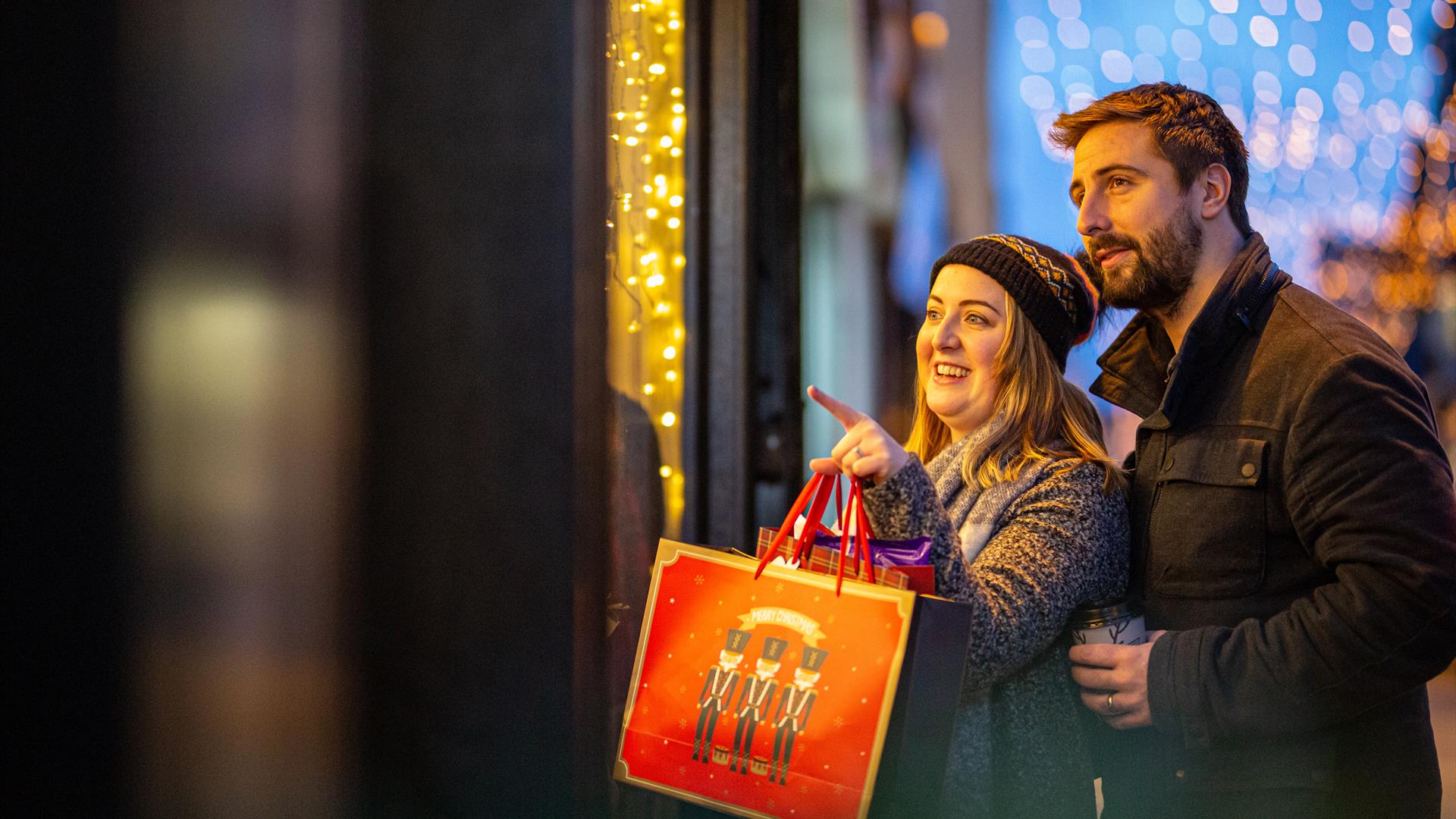 A man and woman shopping together carrying Christmas bag and Christmas lights in background on Carrickfergus High Street