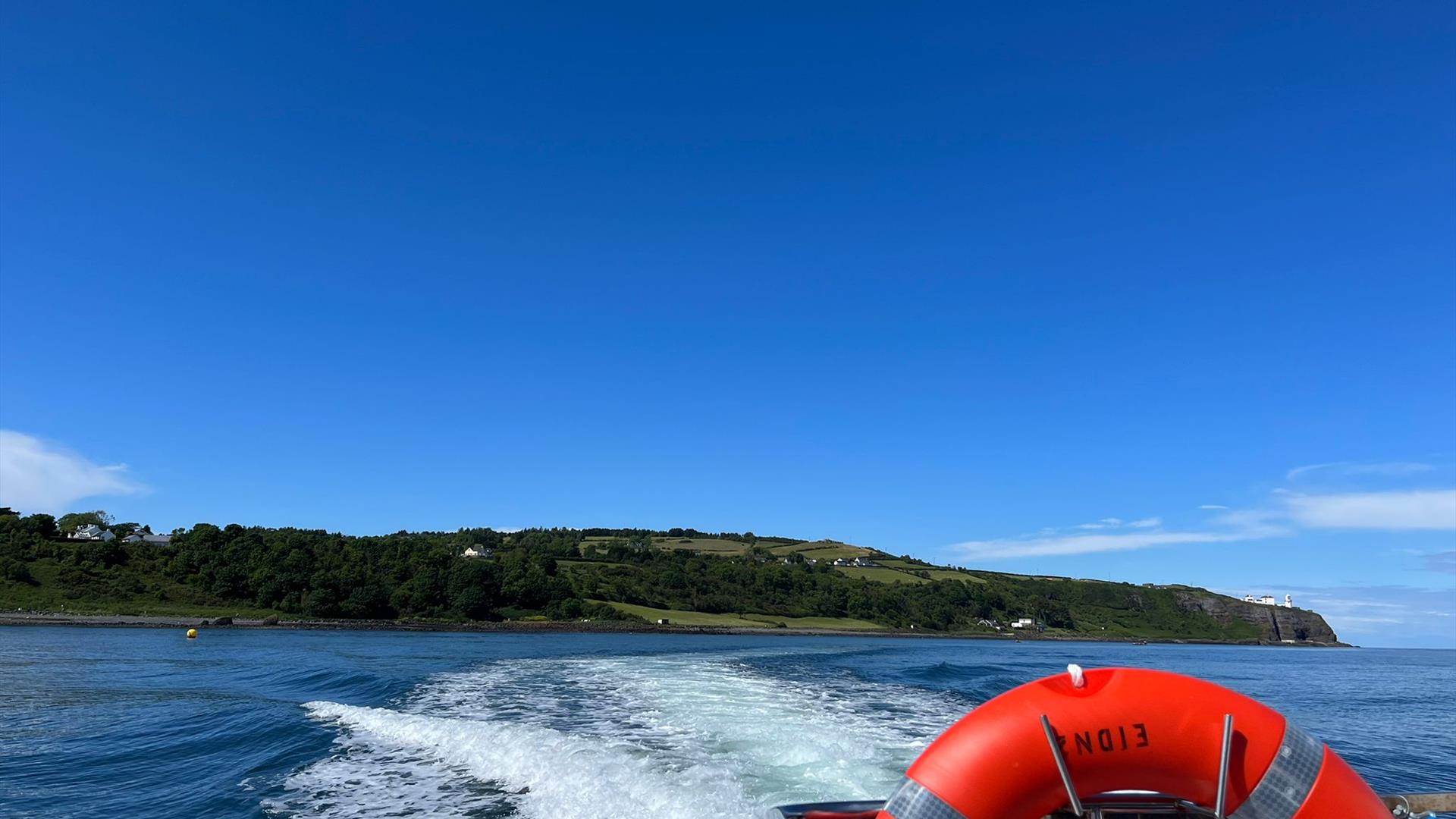 View of Blackhead path and Lighthouse with wake of sea behind boat and life ring visible on Charter NI Boat