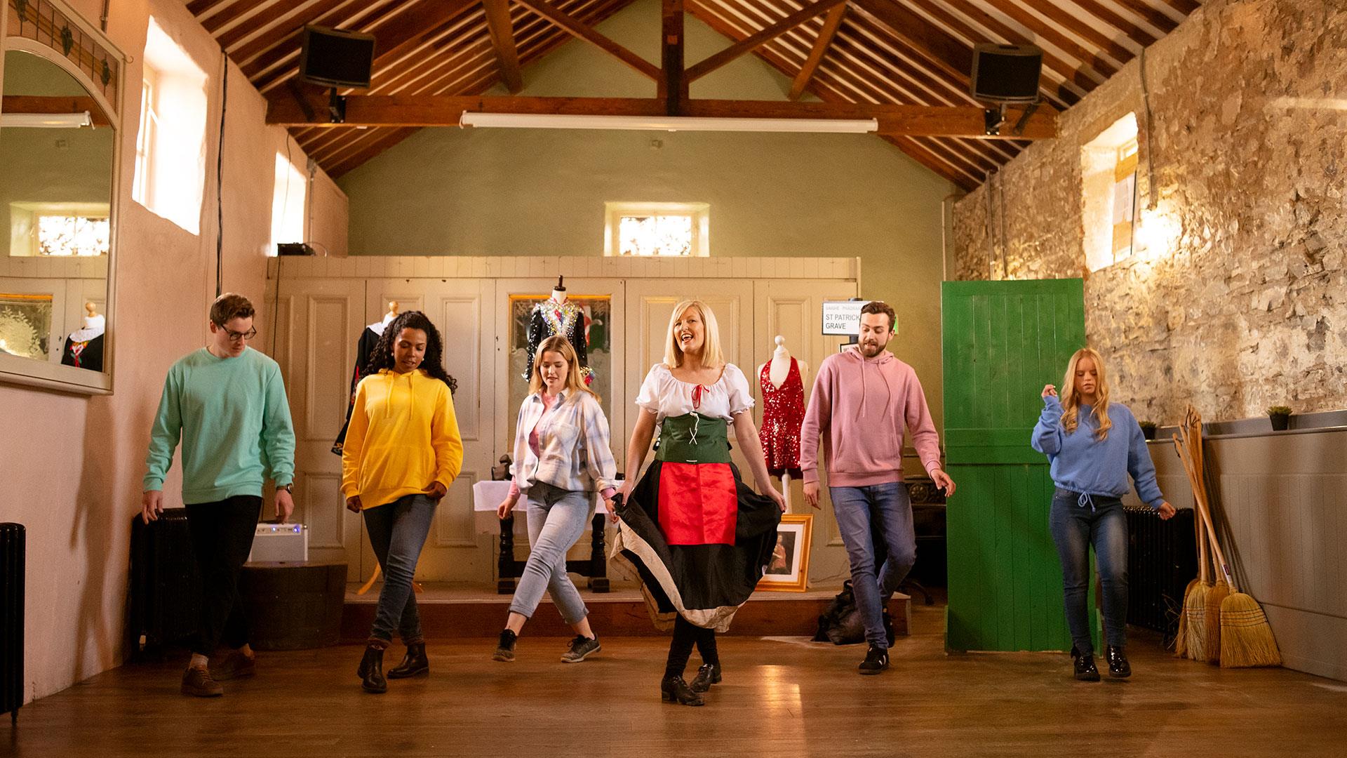 Group in a row with the instructor in front being taught Irish dancing as part of the Dancing at the Crossroads experience