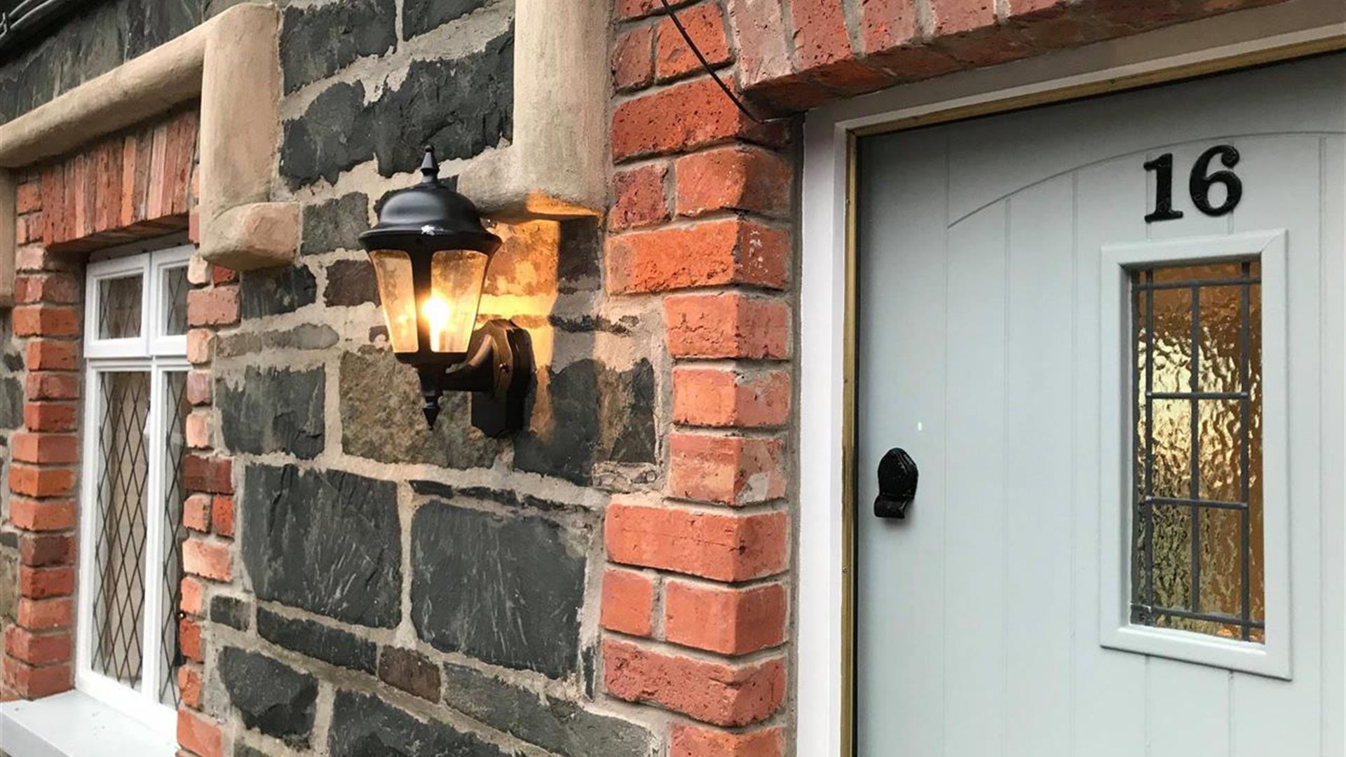 Image shows front door of No 16 with lantern on the brick wall outside