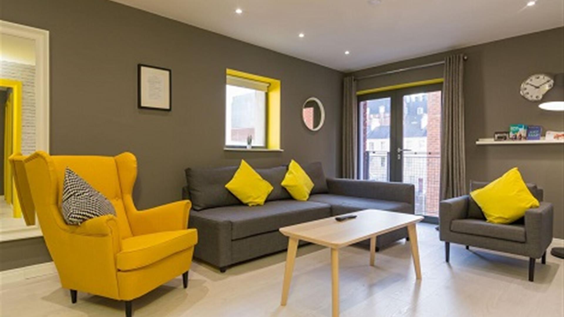 A grey sitting room with grey and yellow chairs, a grey sofa and a coffee table.