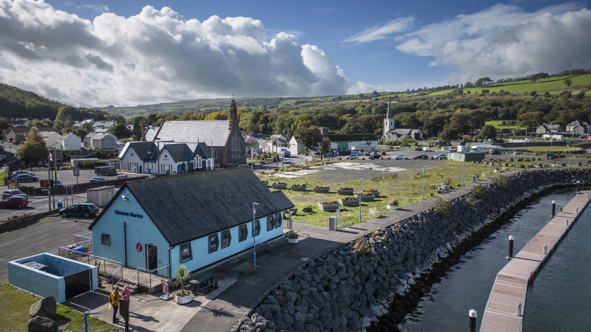 Aerial view of blue Glenarm Tourism building with town in the background and marina jetty in the foreground