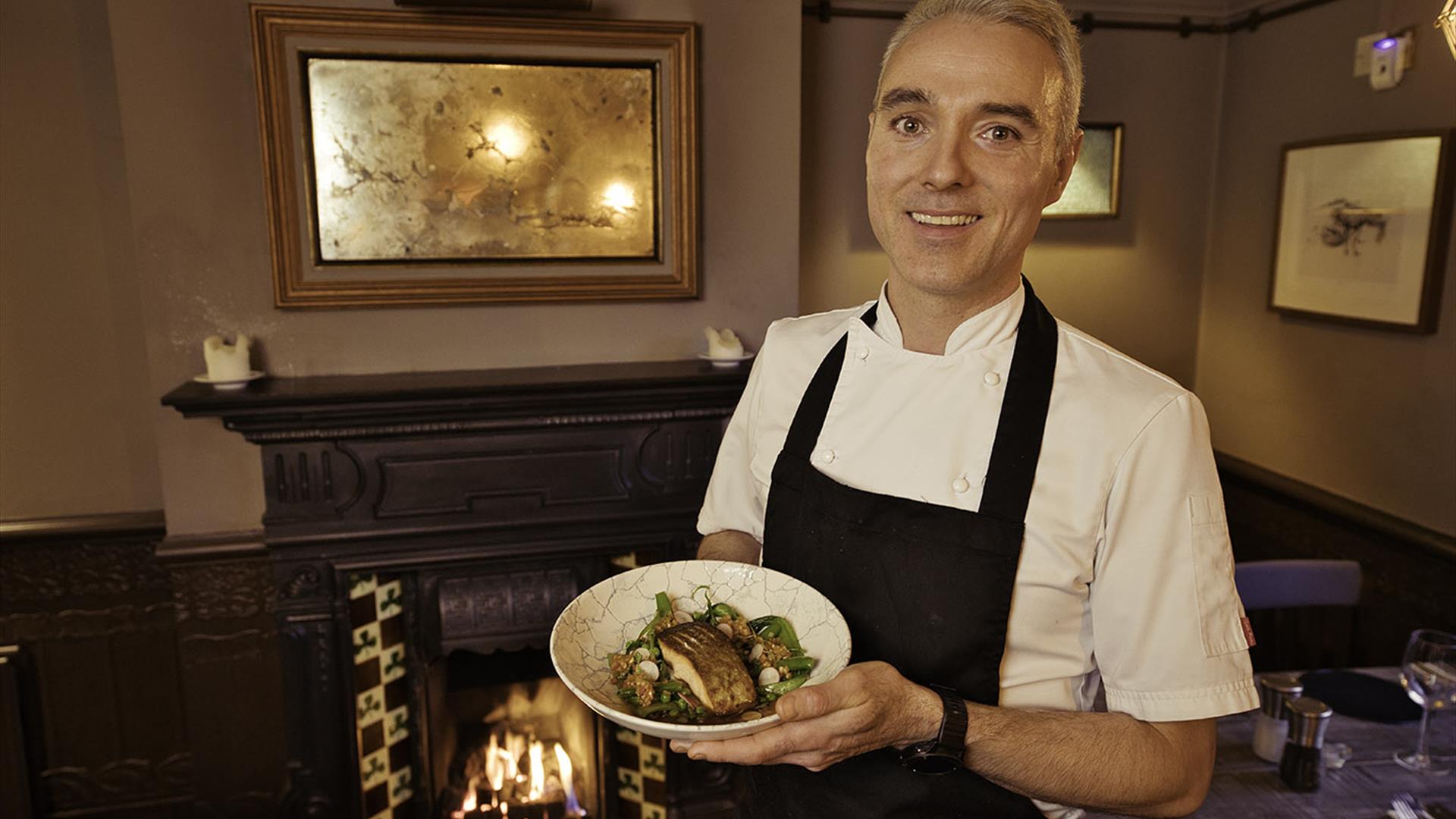 Chef holding a plate of food in front of an open fire