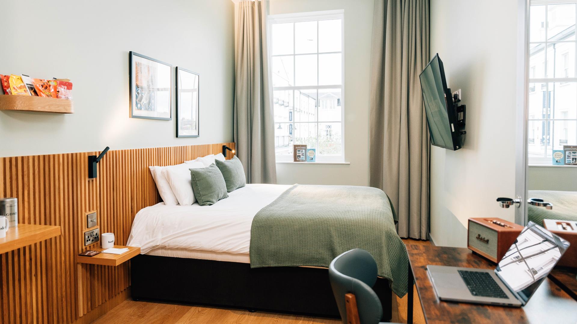 Image shows a double bed in a hotel room with paintings of Northern Ireland on the background wall