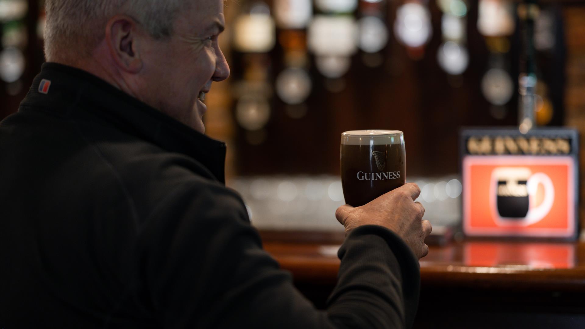 Gentleman drinking a freshly poured pint of Guinness in a branded glass at the bar of Charlie's Bar Enniskillen