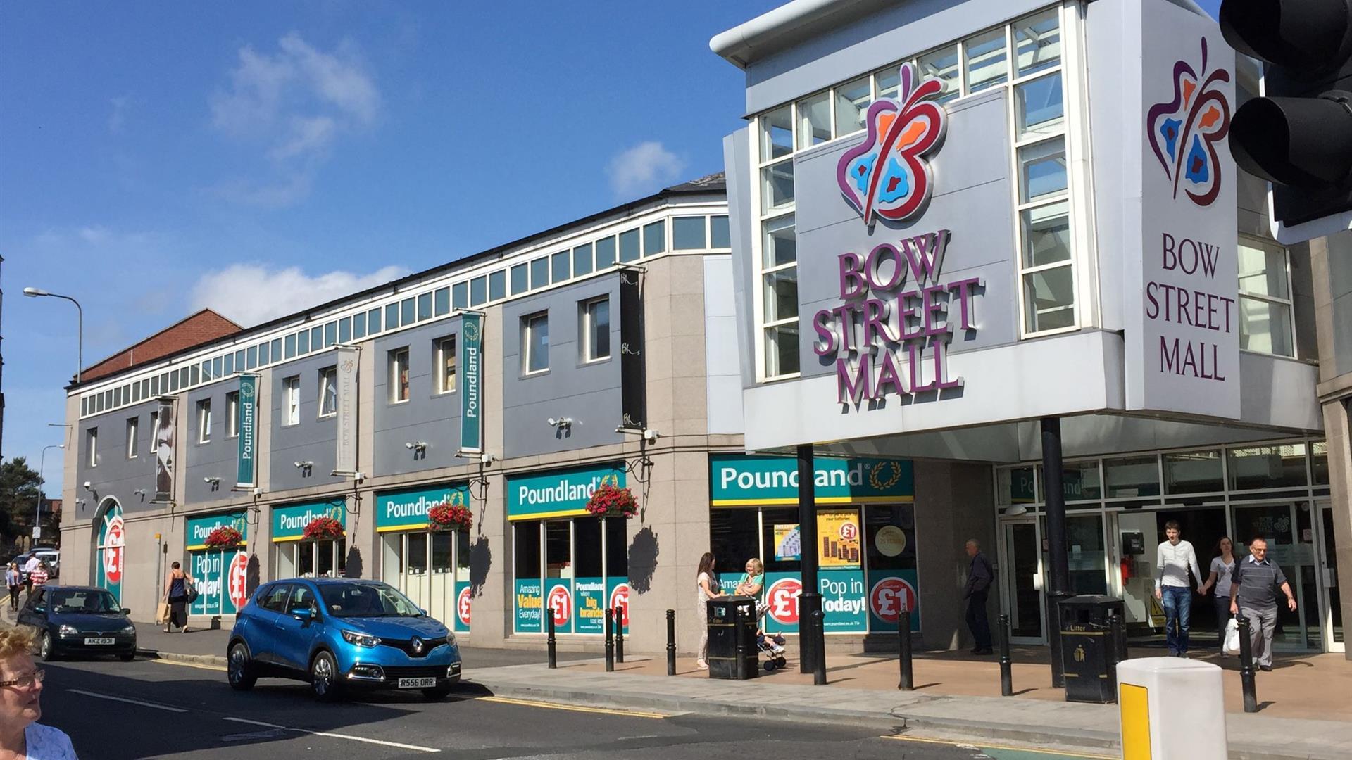 Image shows entrance to Bow Street Mall with visitors exiting the mall and cars driving by