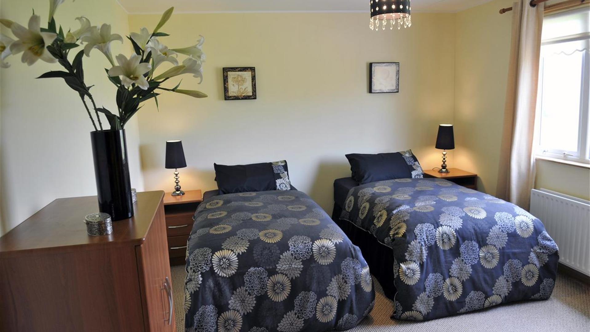 Twin bedroom with 2 single beds with bedside lockers and bunch of flowers in image