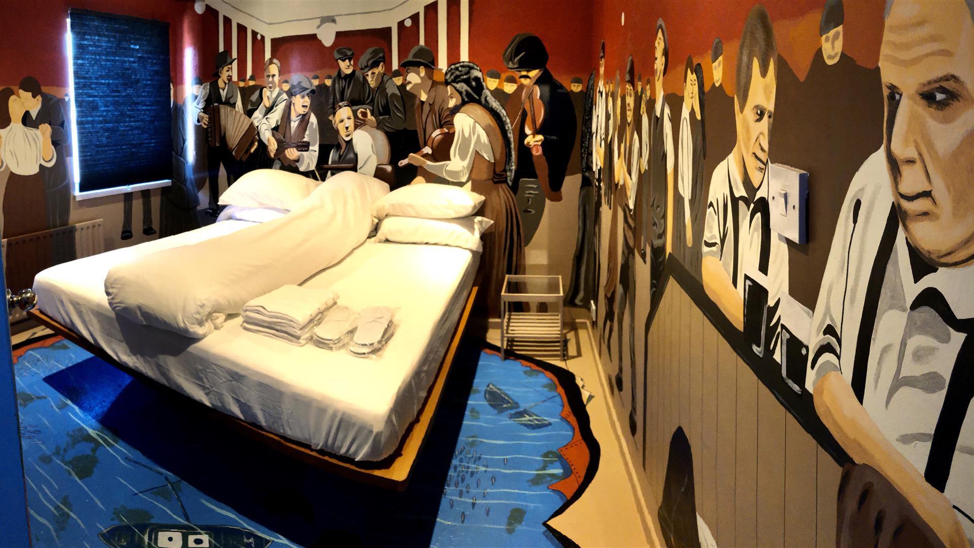 A photo of a Titanic-themed bedroom with murals of passengers on the ship, surrounding a double bed.