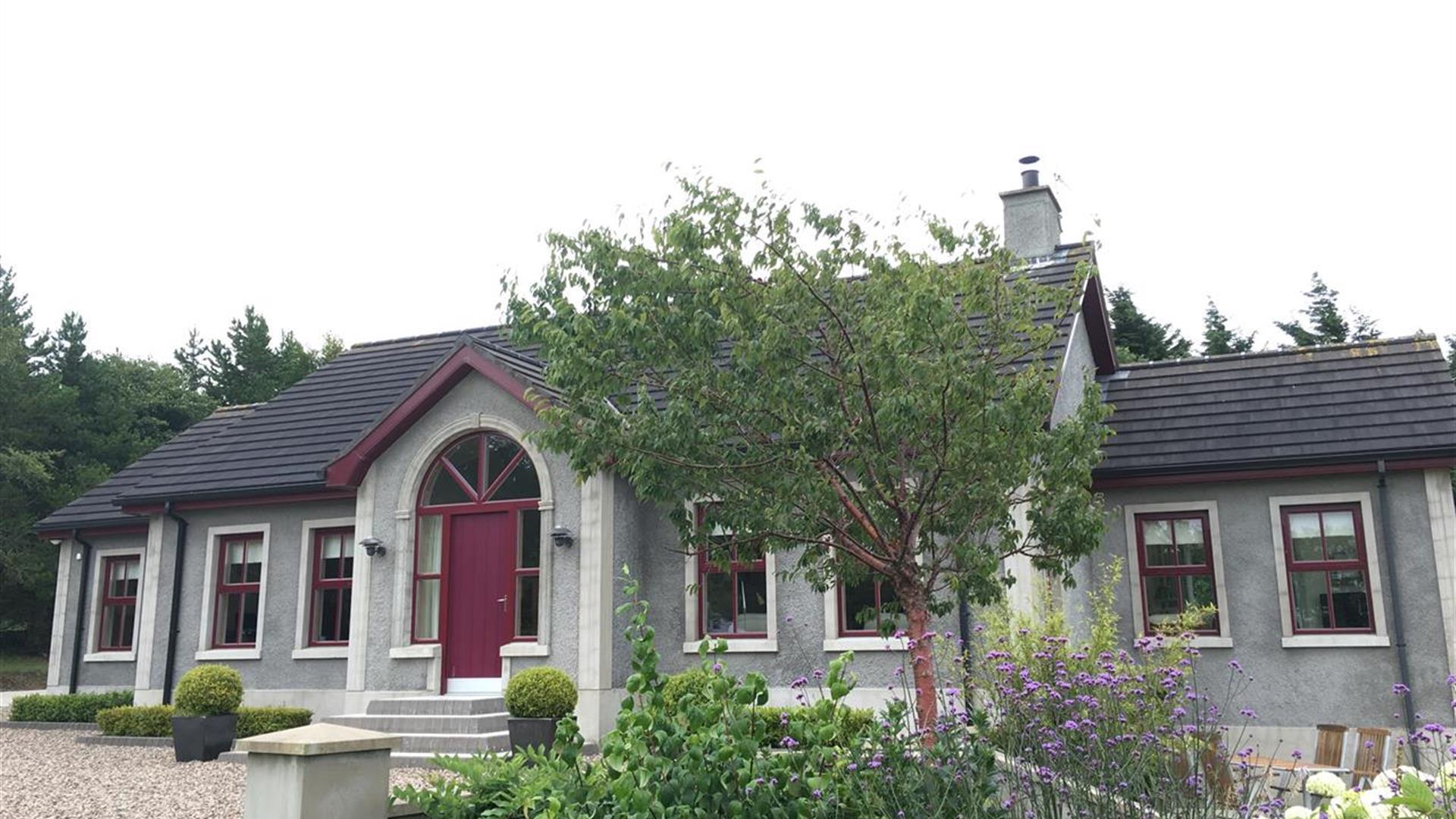 The front exterior of a B&B house with potted plants lining the front of the house and a garden with a tree and flowers.