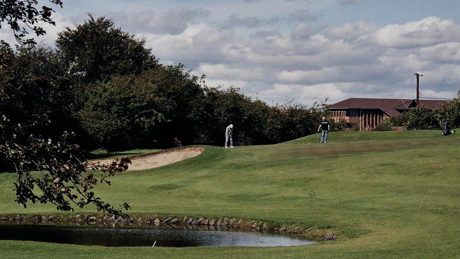 Men playing golf on a course with a pond and a sand bunker.