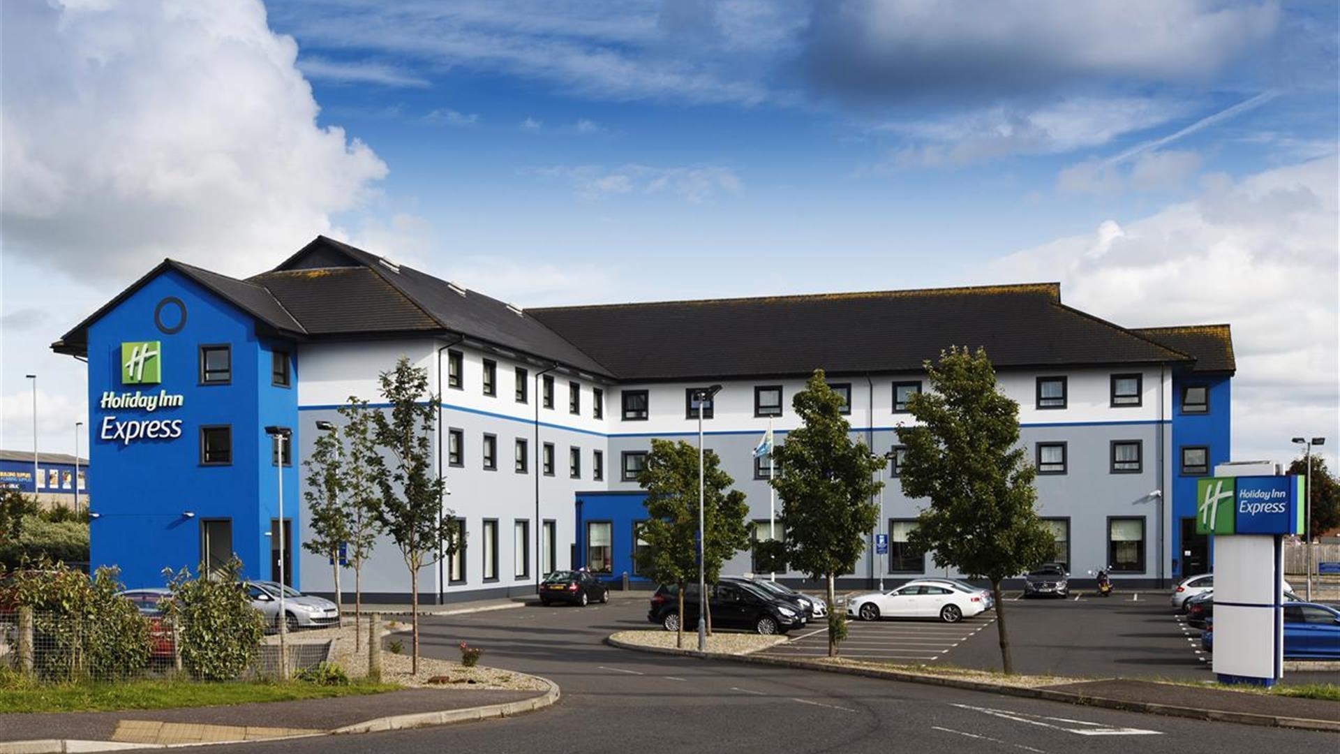 A large blue three floor hotel with a car park.