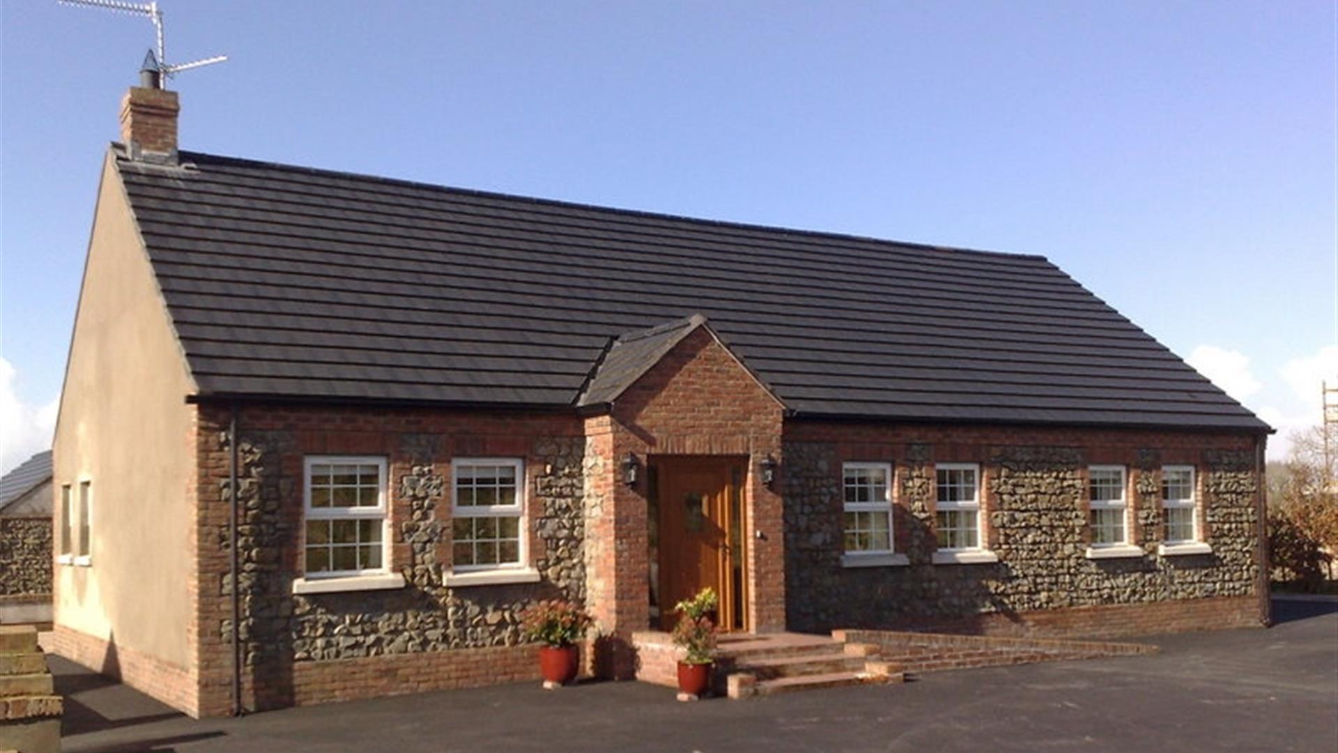 Image shows front of detached cottage which has 6 windows and front door with a few low steps