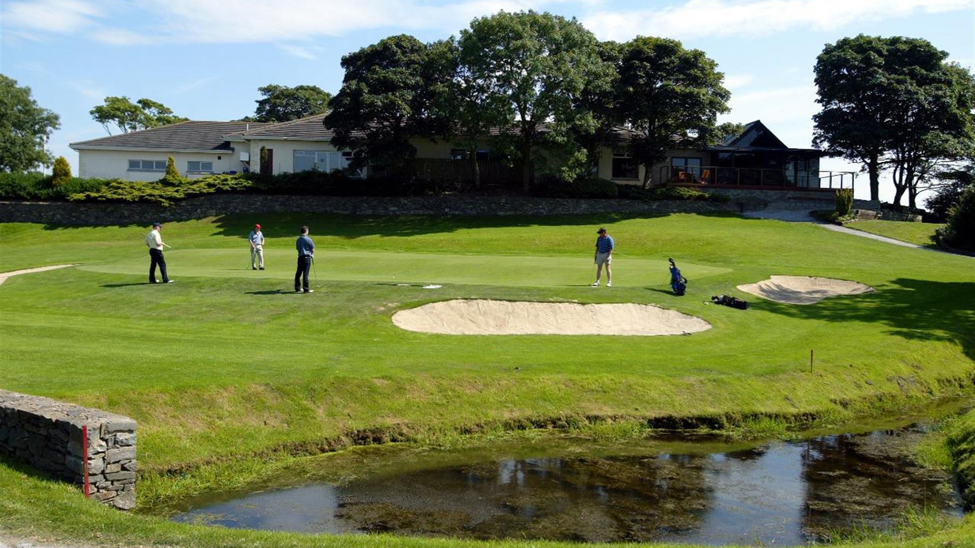 Image is of golf course with golfers playing and lake in the foreground