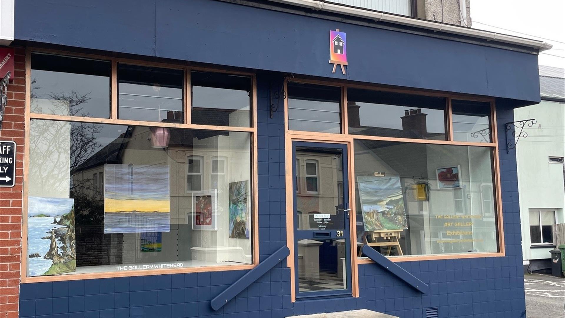 Exterior of the Gallery in Whitehead, painted blue with large windows and art displayed in them