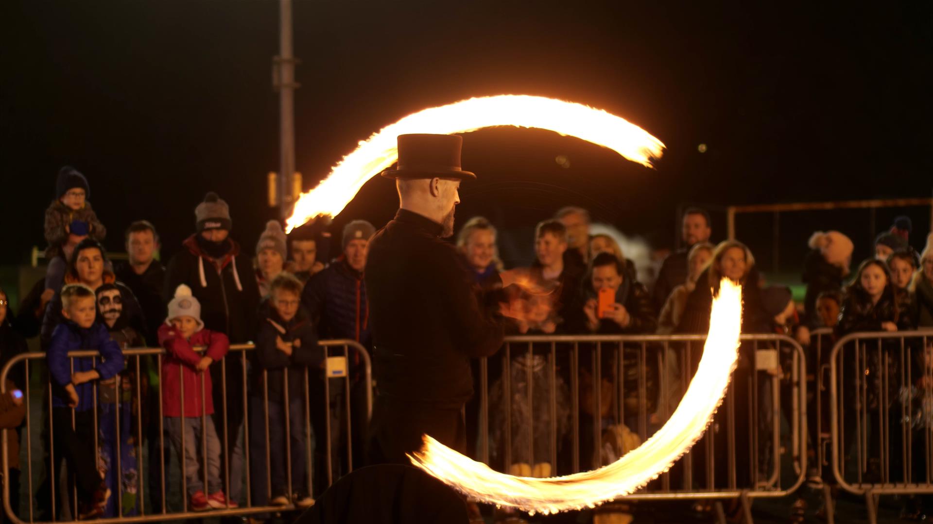 Image shows a man with fire poi entertaining the crowd