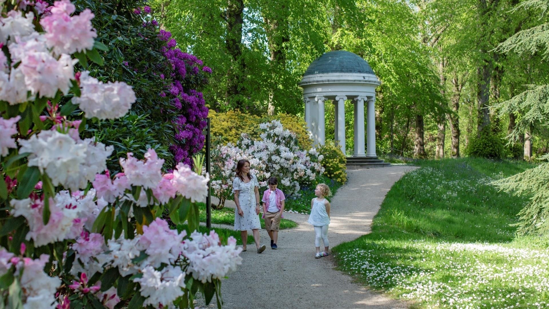 Image shows flowers in bloom at gardens of hillsborough castle with two children and an adult walking along