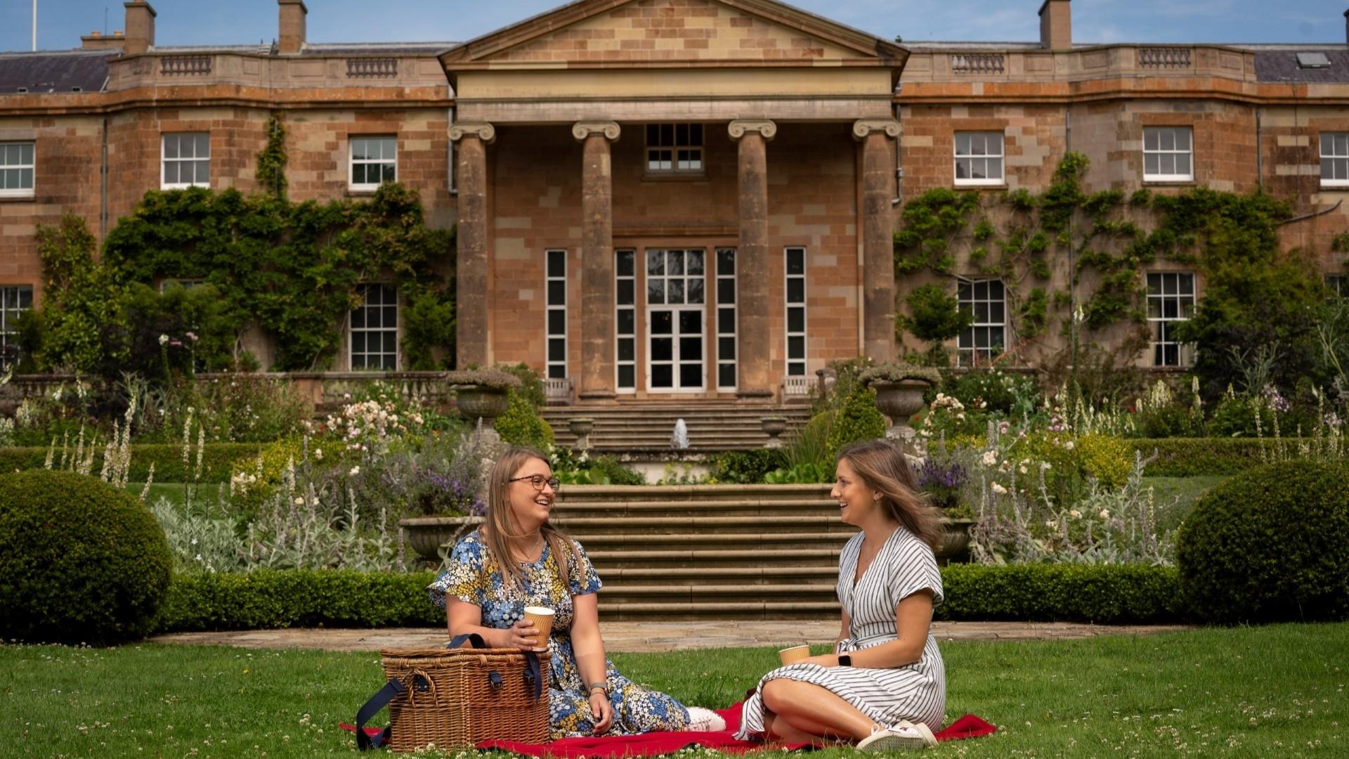 Image is of 2 girls sitting on the lawn at Hillsborough Castle