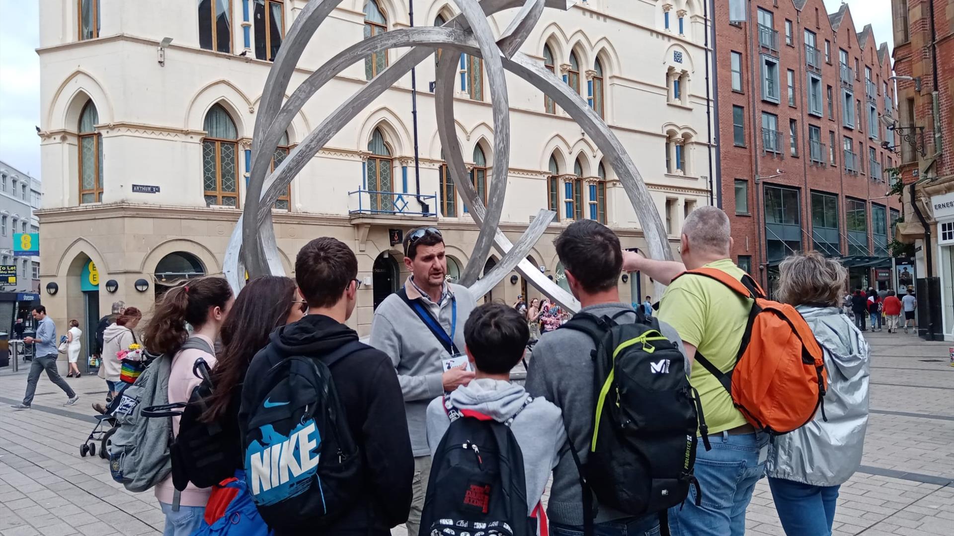 A tour group listening to a guide at a sculpture in Belfast city centre.